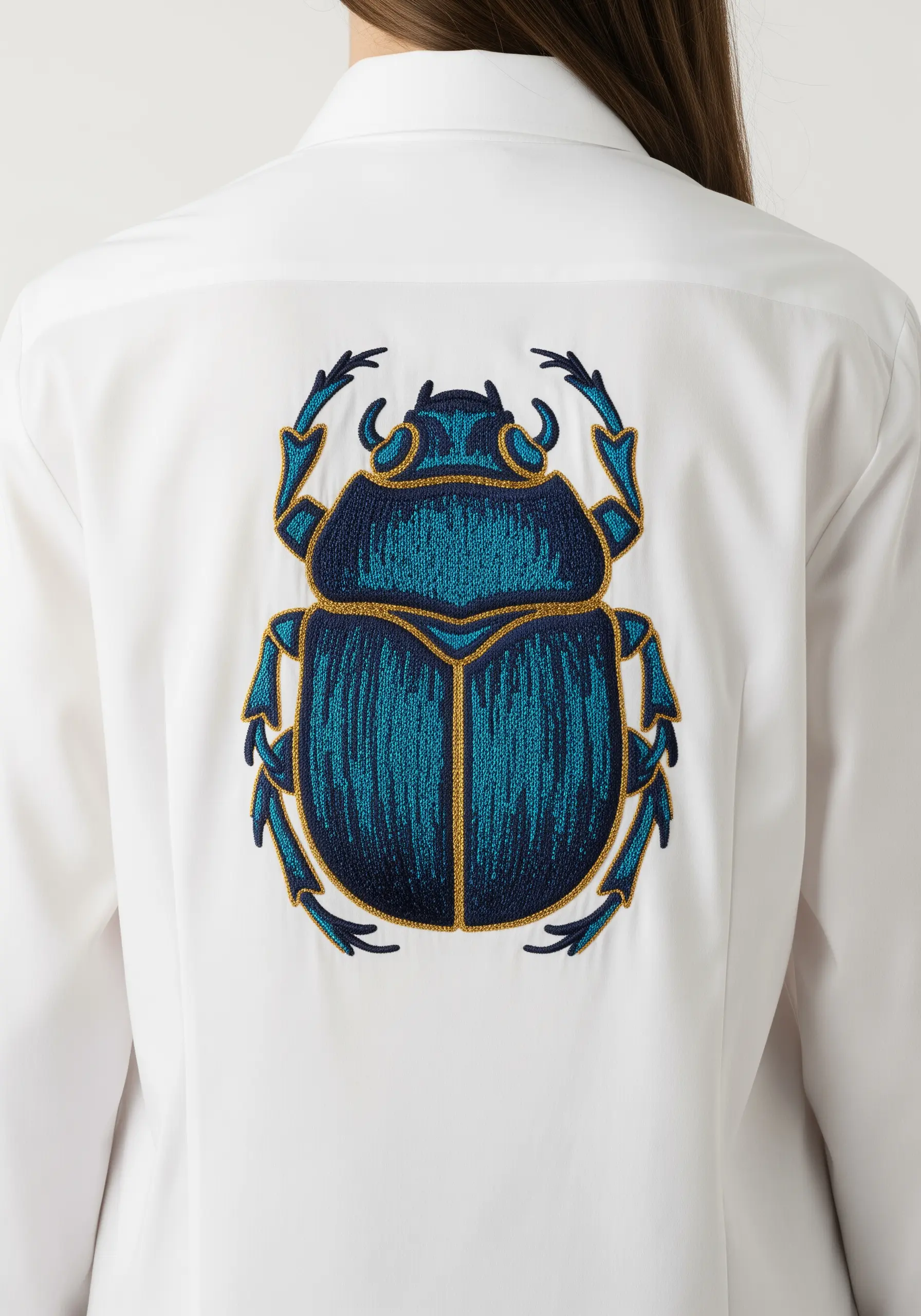Large teal and blue scarab beetle with a gold outline embroidered on a white shirt.