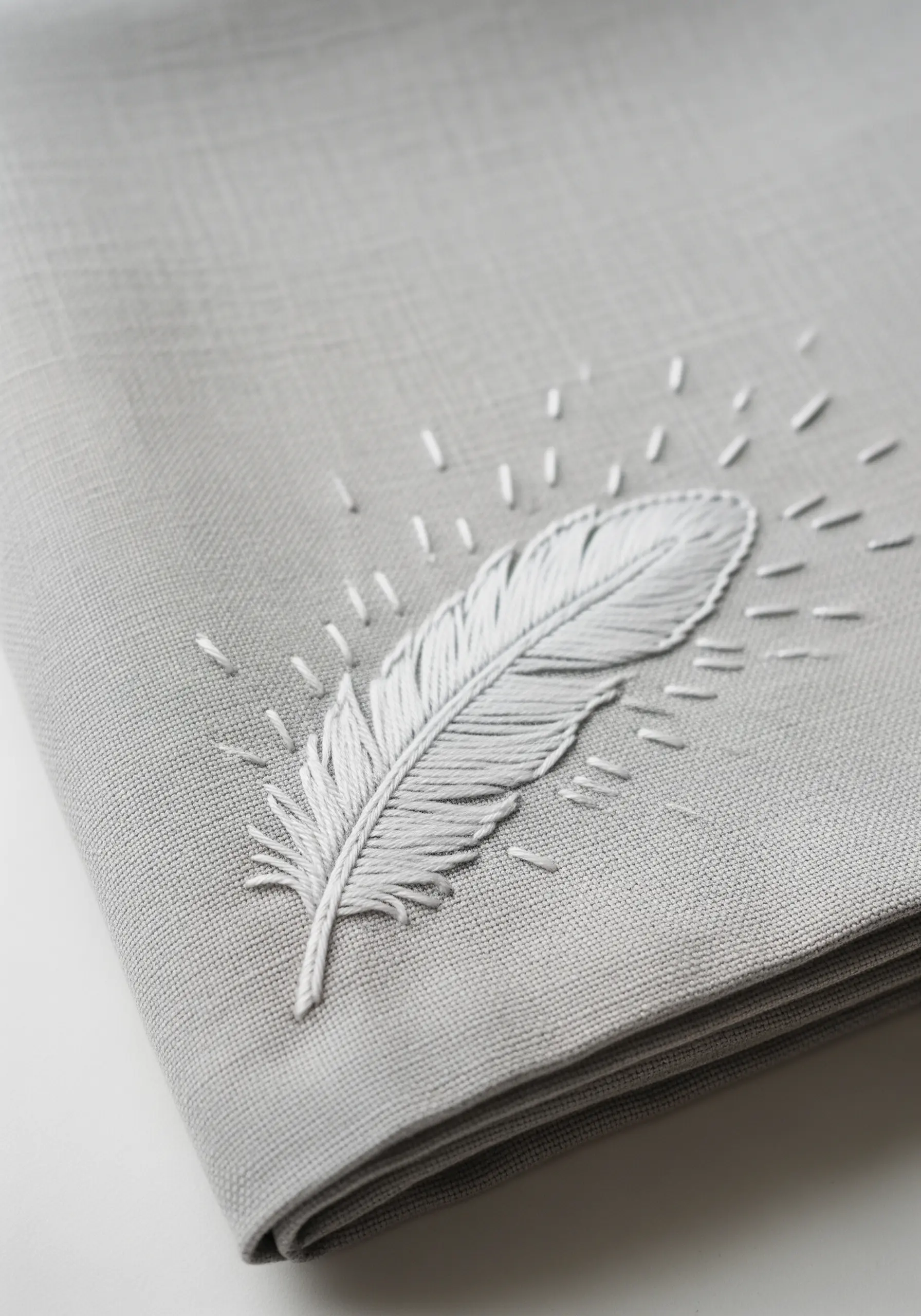 A detailed white feather embroidered with fishbone stitch on gray fabric.