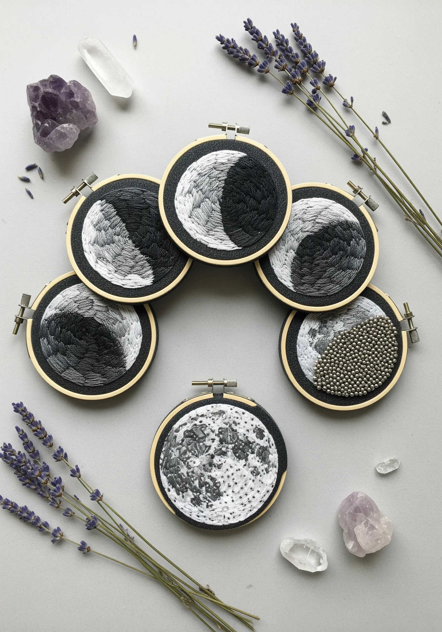 A collection of small embroidery hoops showing different phases of the moon in grey and white.