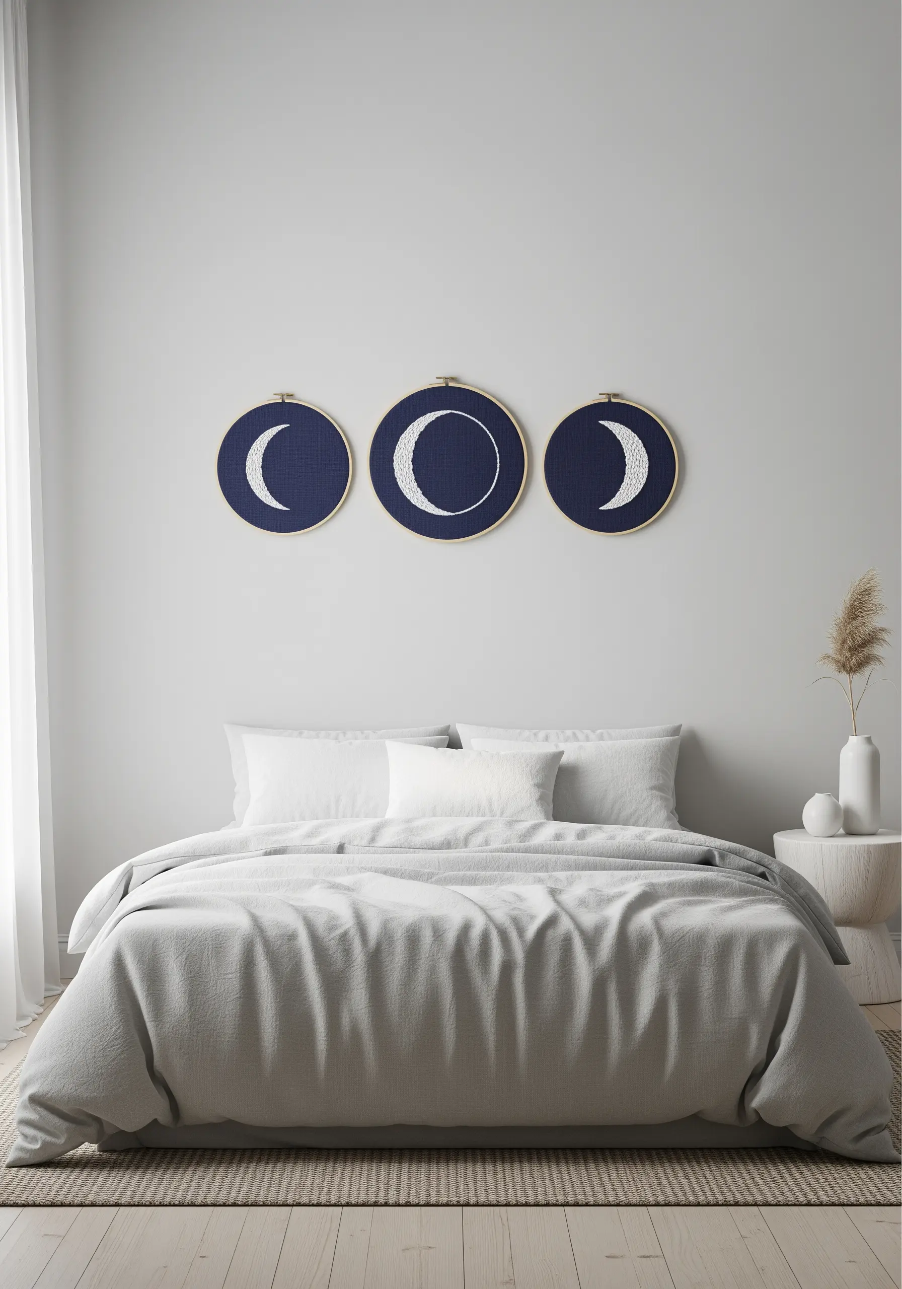 Three embroidery hoops displaying the phases of the moon, stitched in white on navy fabric.