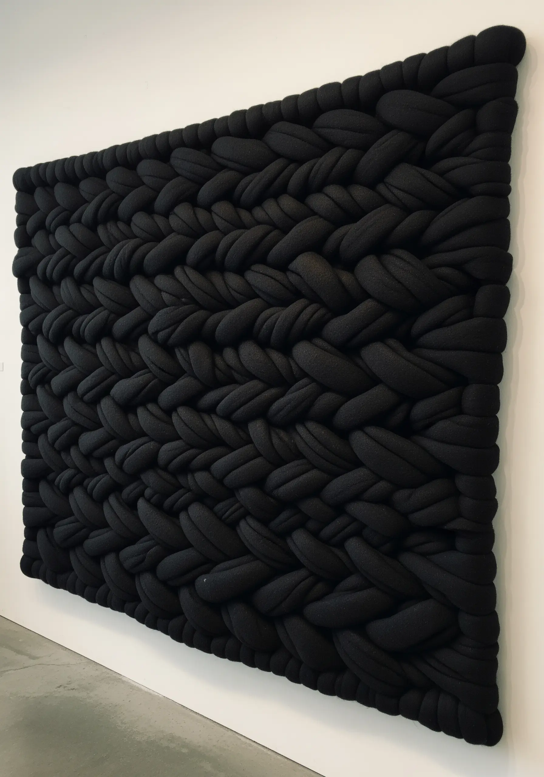 A large, all-black wall hanging made from extremely thick, braided tube yarn.
