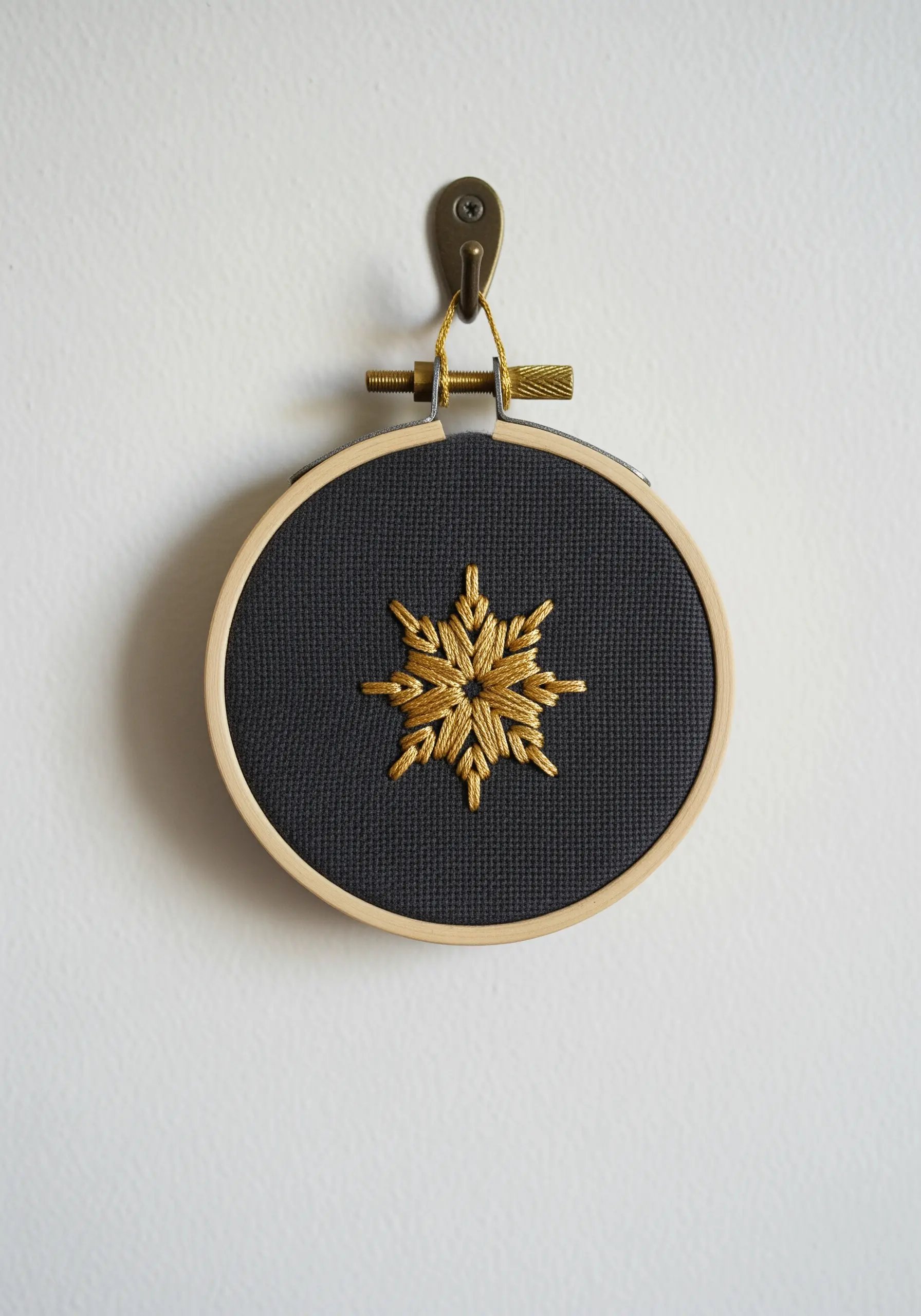 A small gold metallic snowflake mandala stitched on dark charcoal fabric.