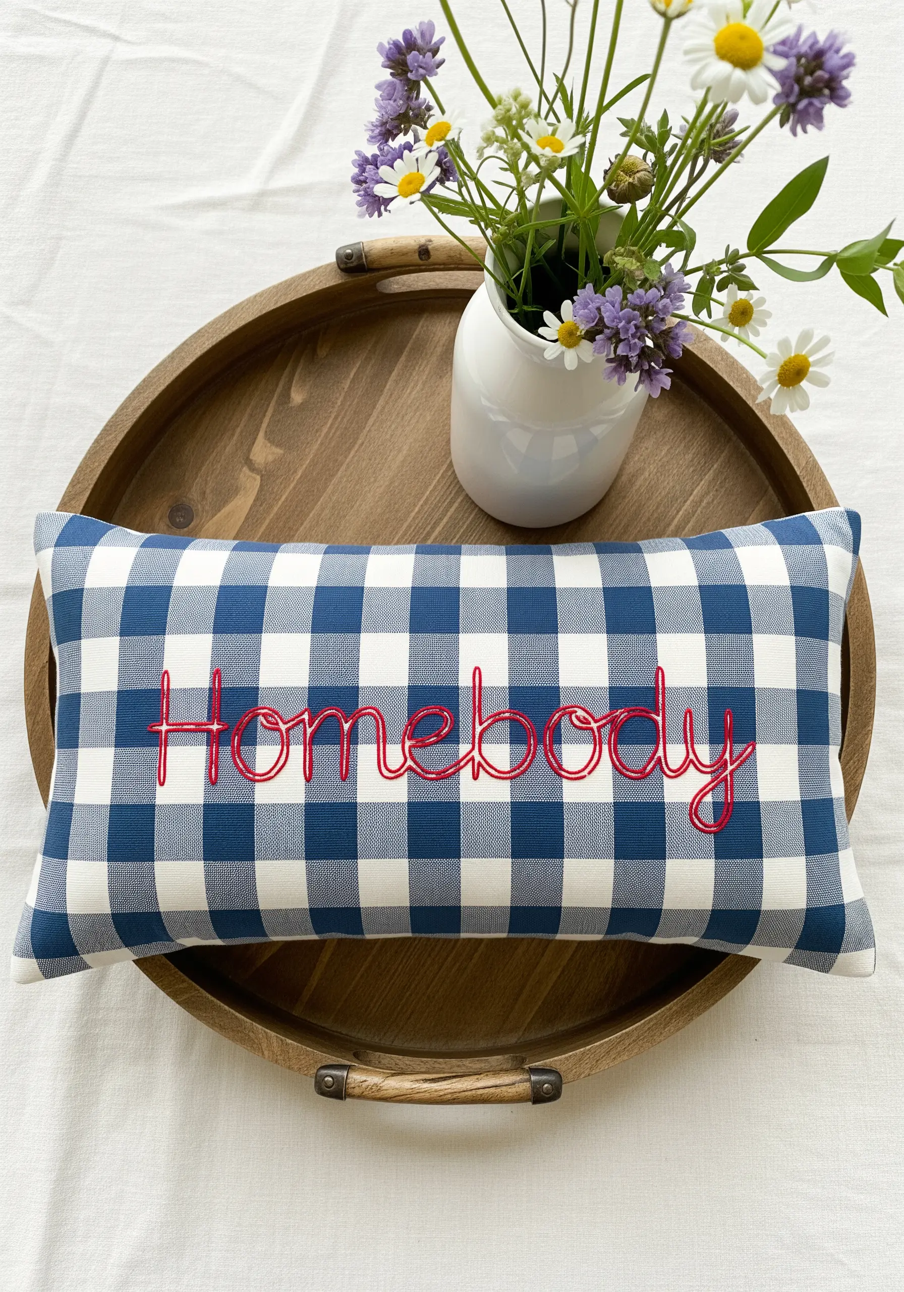 Red chain stitch script spelling 'Homebody' on a blue and white gingham pillow.
