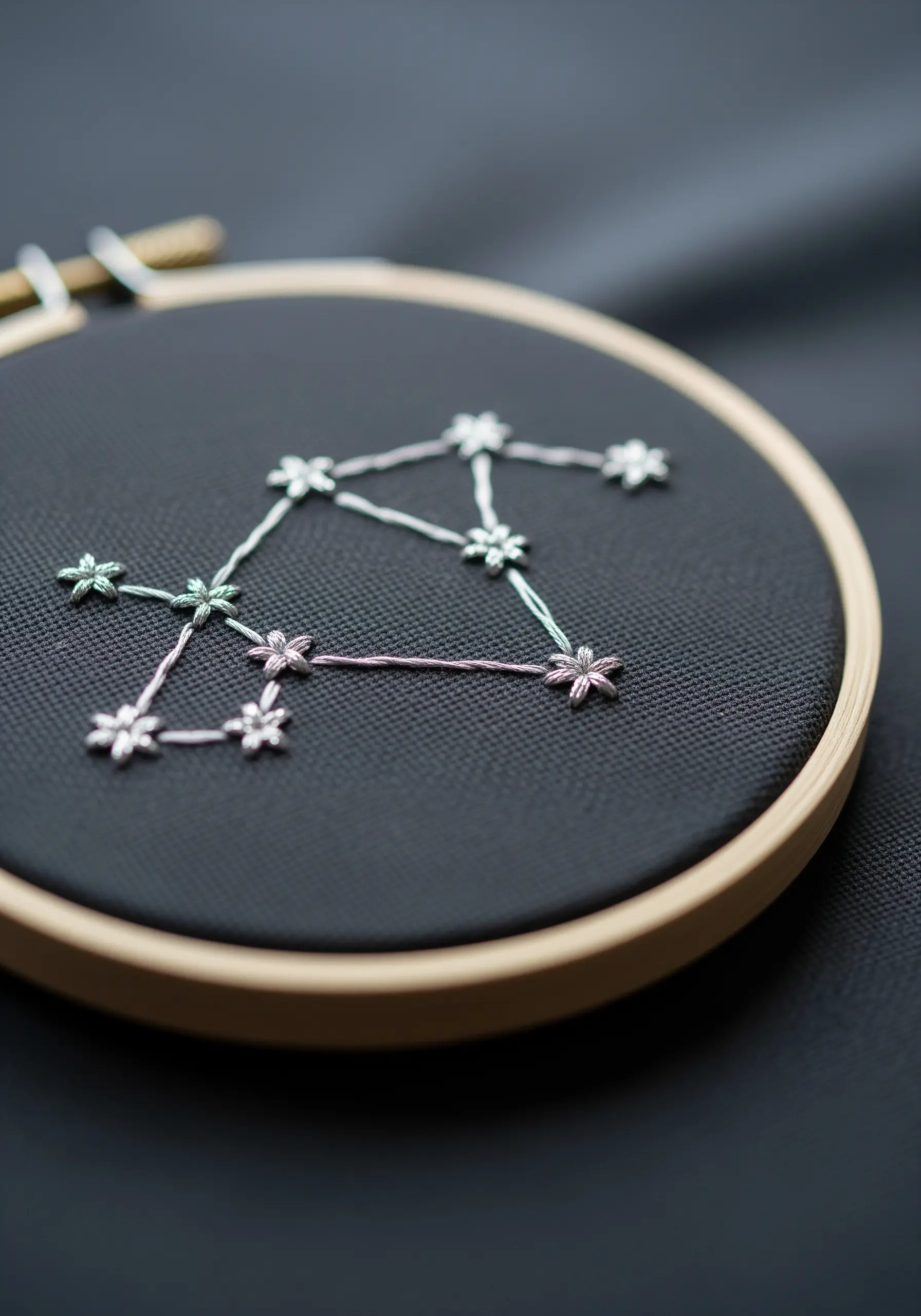 A Libra constellation embroidered with white and pastel thread on black fabric.