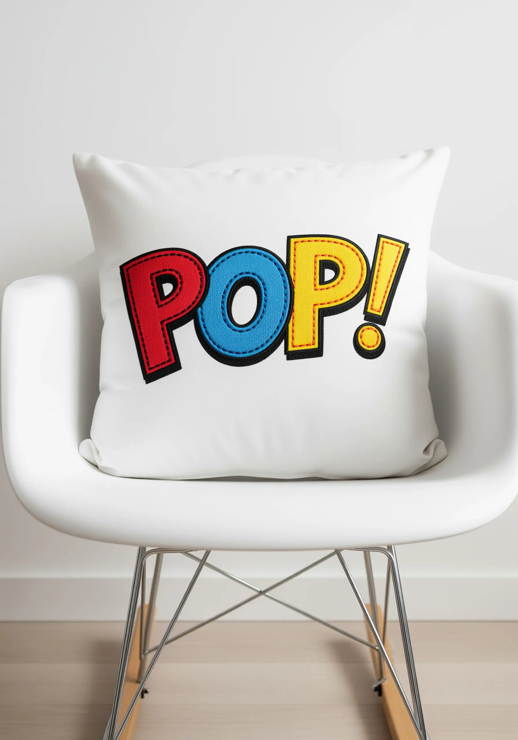 The word POP! in primary color appliqué with black stitch outlines on a white pillow.