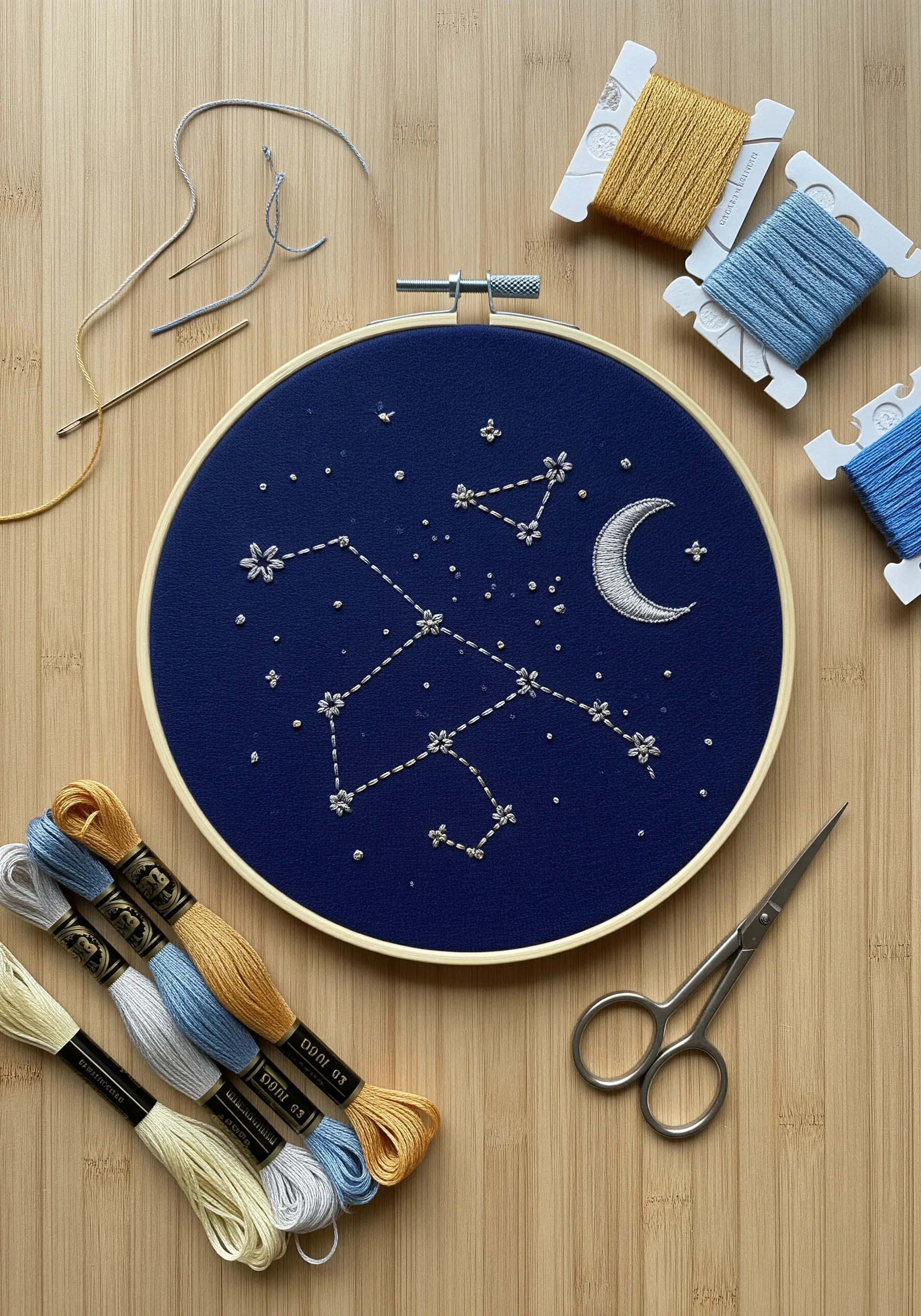 Embroidery hoop with a silver constellation and moon on dark blue fabric.