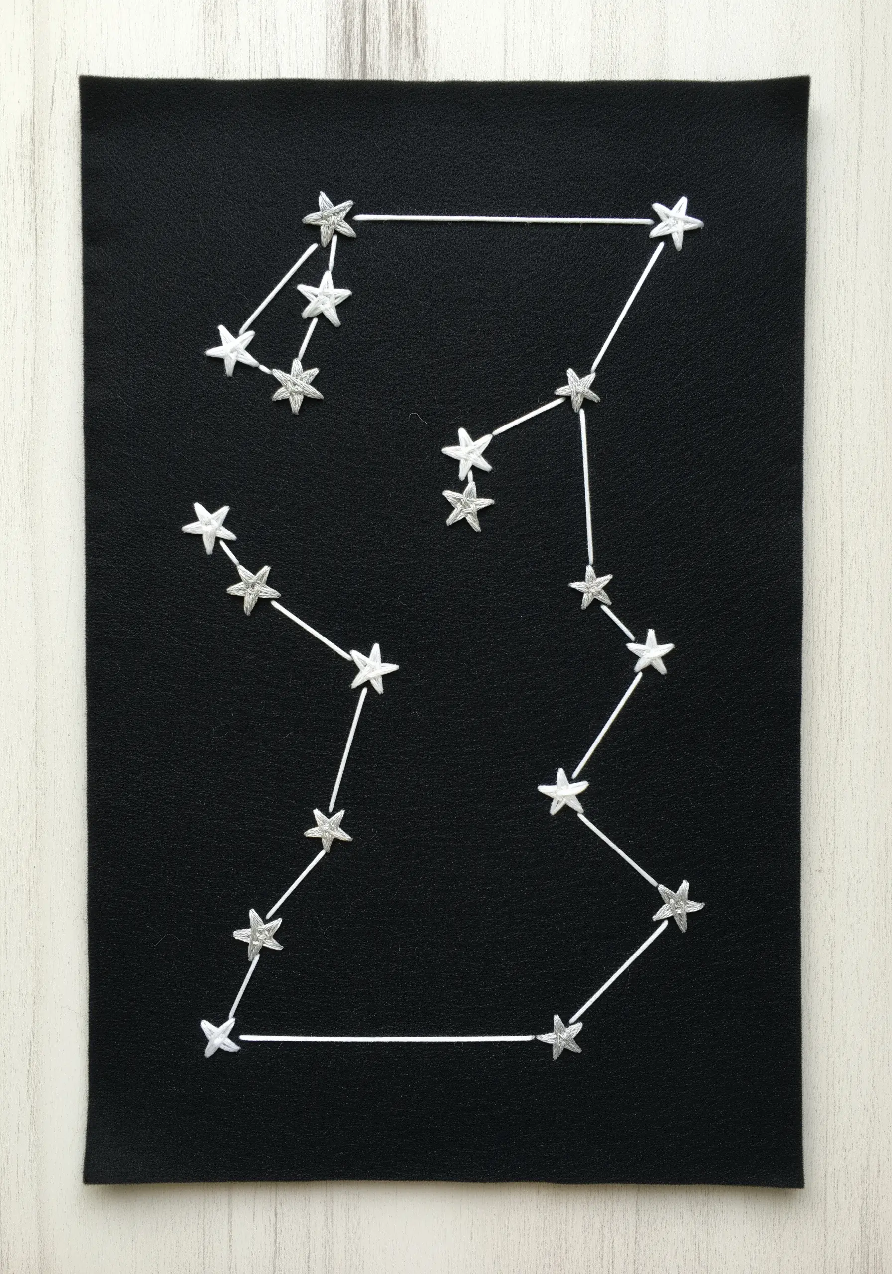 Embroidered constellations on black felt, with silver thread stars connected by white lines.