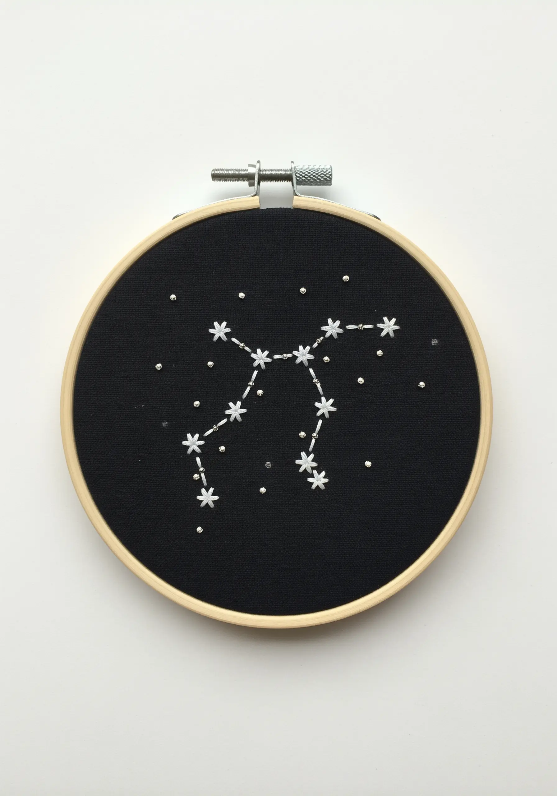 A Gemini constellation embroidered with white French knots and connecting lines on black fabric.
