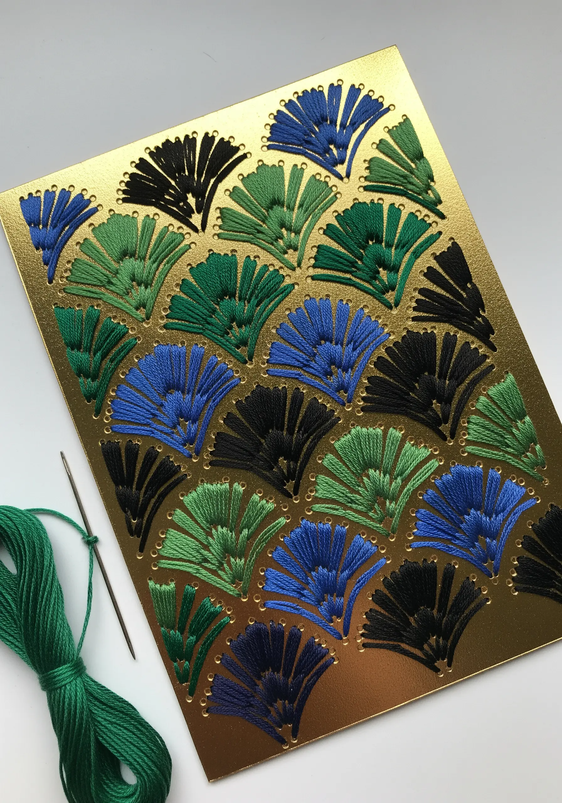 Geometric fan shapes stitched in green, blue, and black on shiny gold cardstock.
