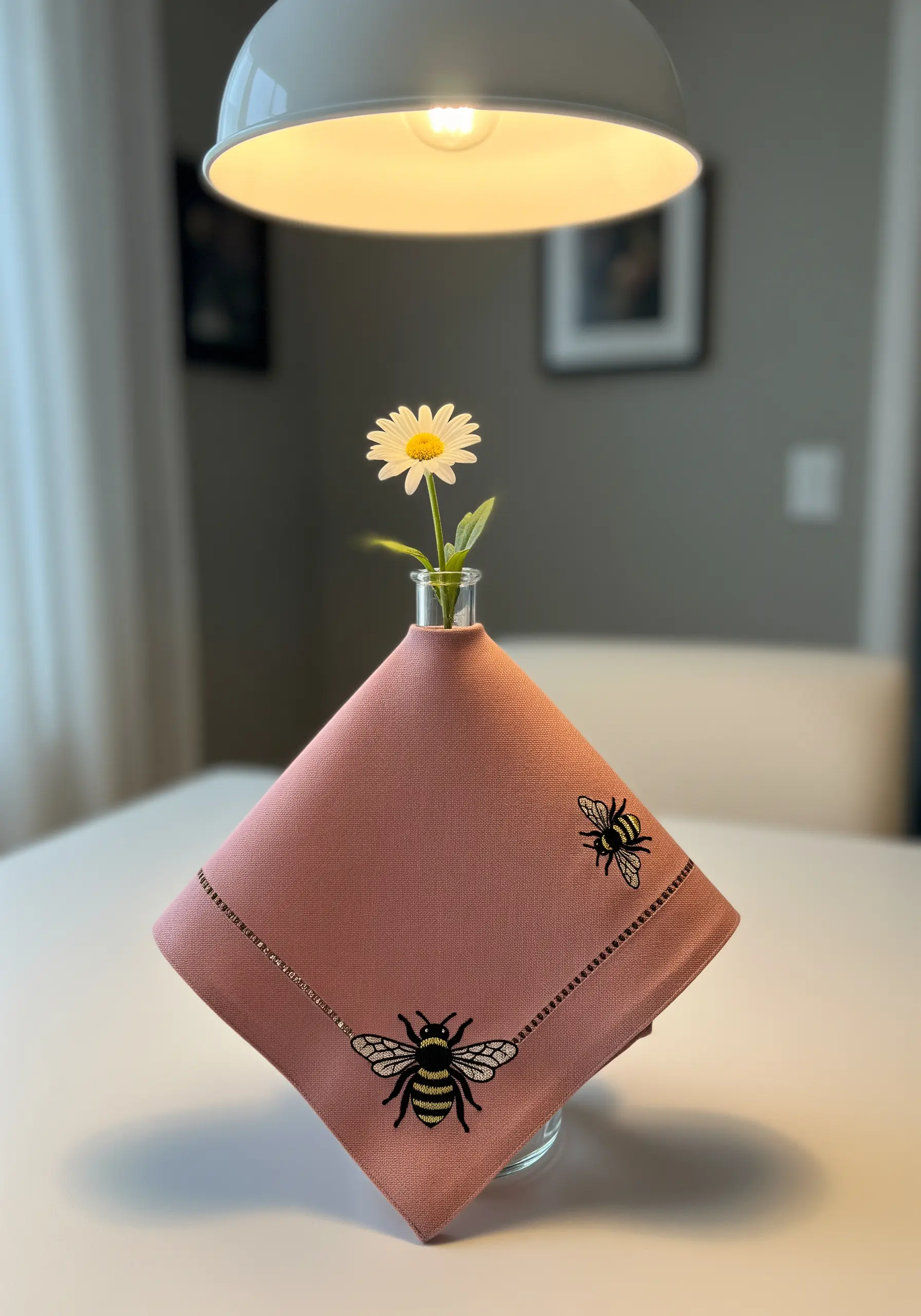 A pink linen napkin with two small, detailed embroidered bees and a beaded border.