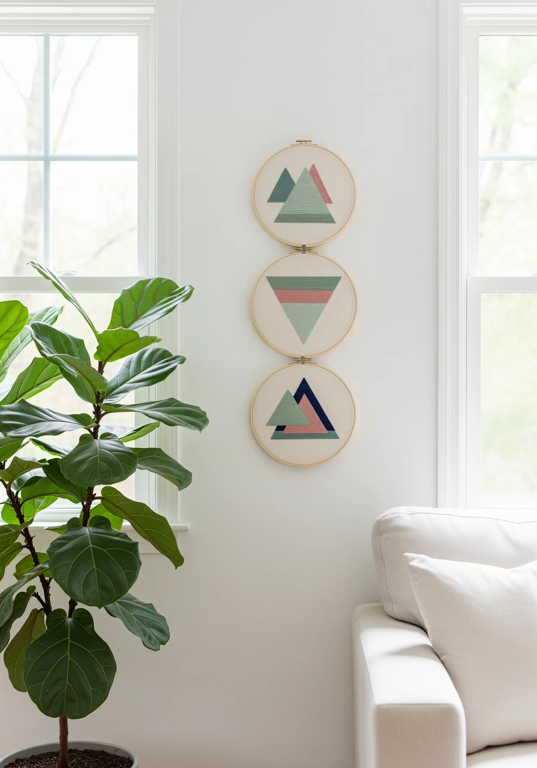 Triptych of three embroidery hoops with pastel green and pink geometric triangle designs.