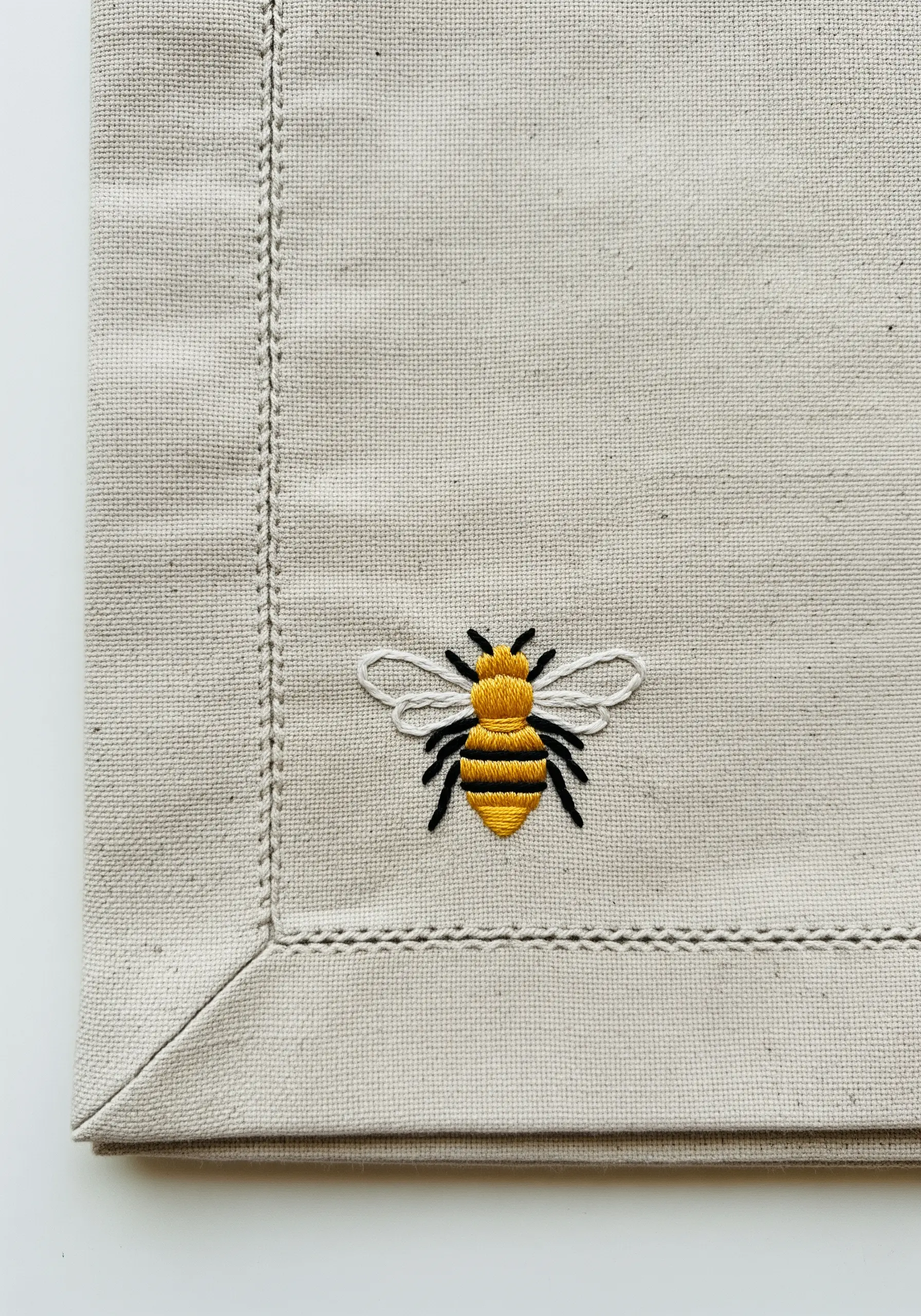 Small embroidered bee with yellow and black satin stitch stripes on a linen napkin.