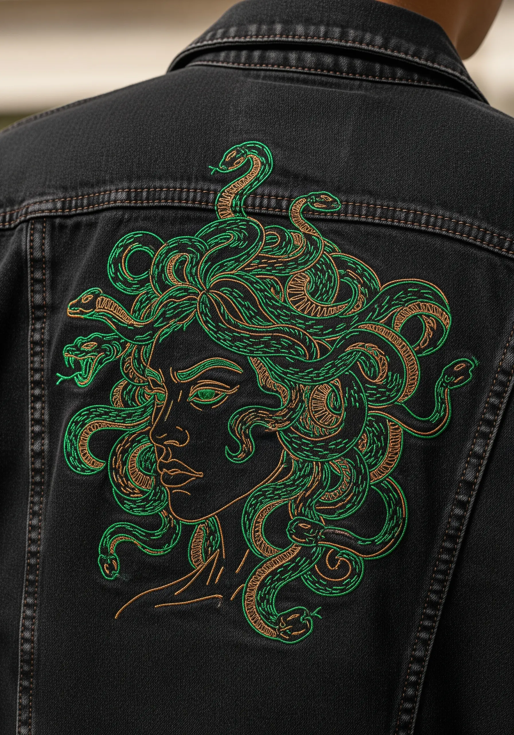 Intricate Medusa portrait embroidered on a black jacket using green and copper metallic thread.