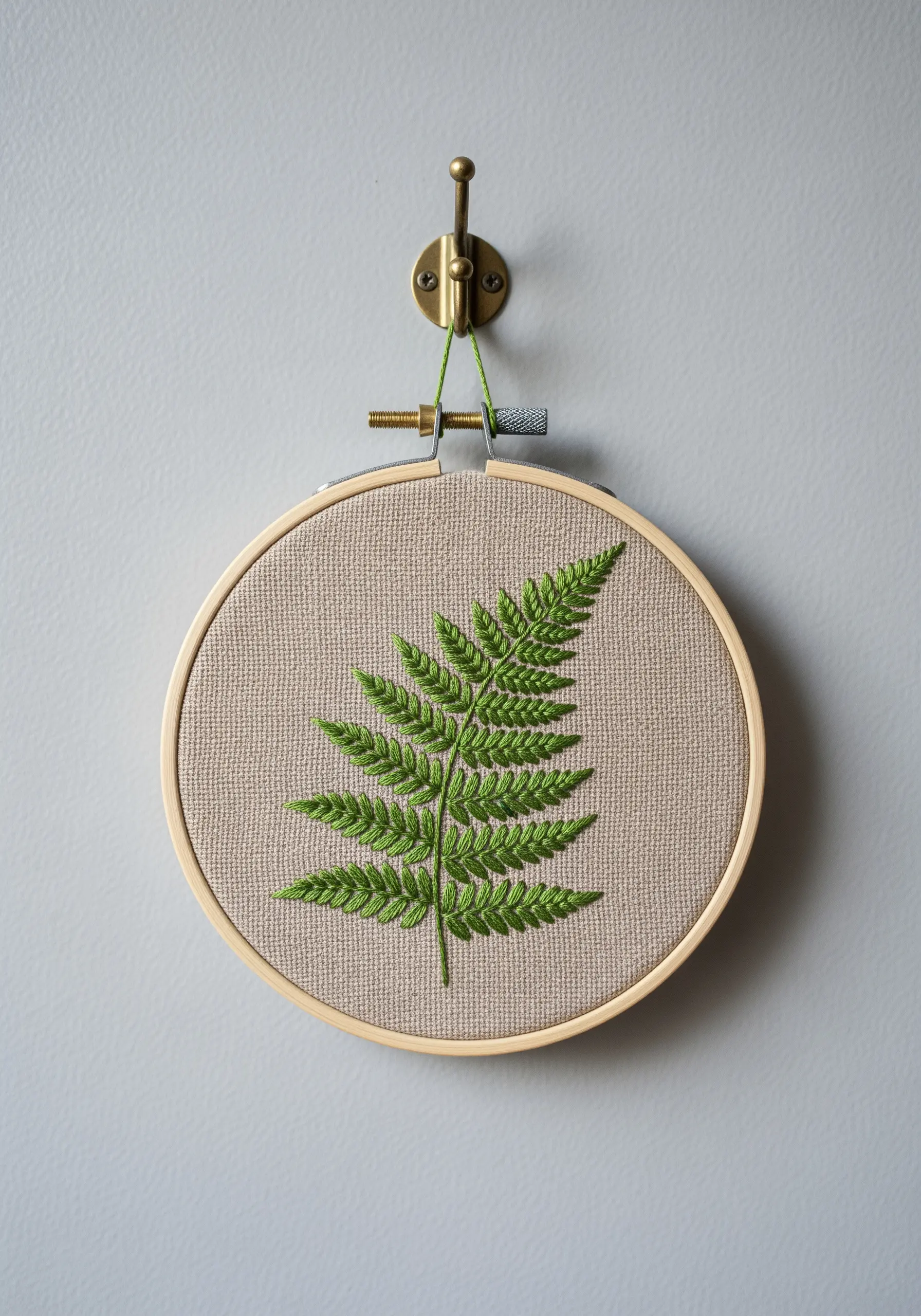 A realistic green fern leaf embroidered on neutral linen fabric.