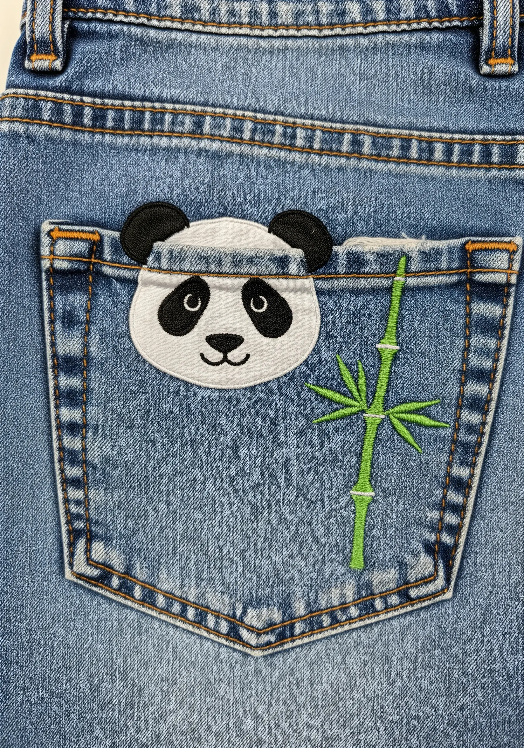 A small panda face appliqué peeking out of the back pocket of a pair of blue jeans.