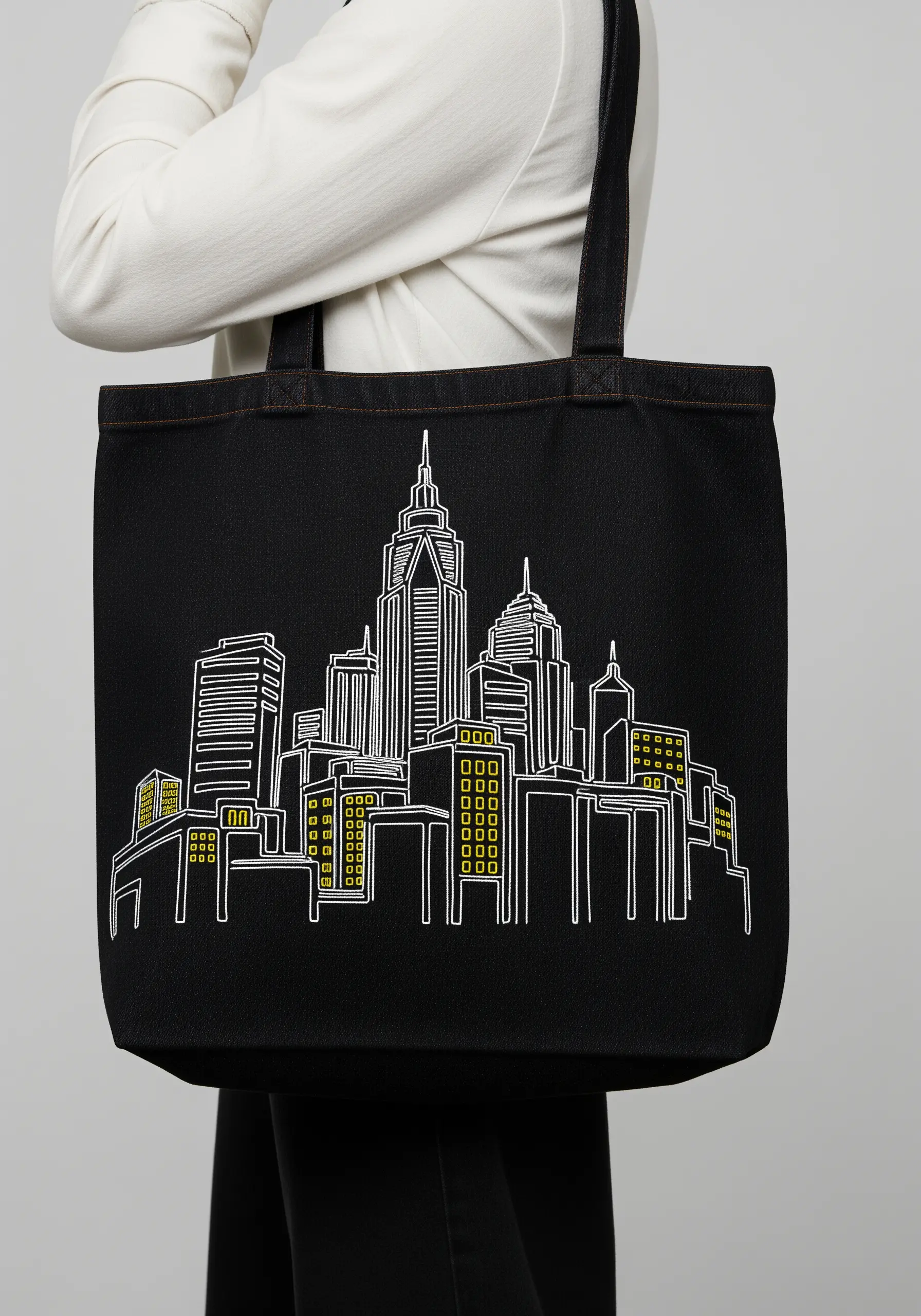 A minimalist white line art embroidery of a city skyline on a black tote bag.