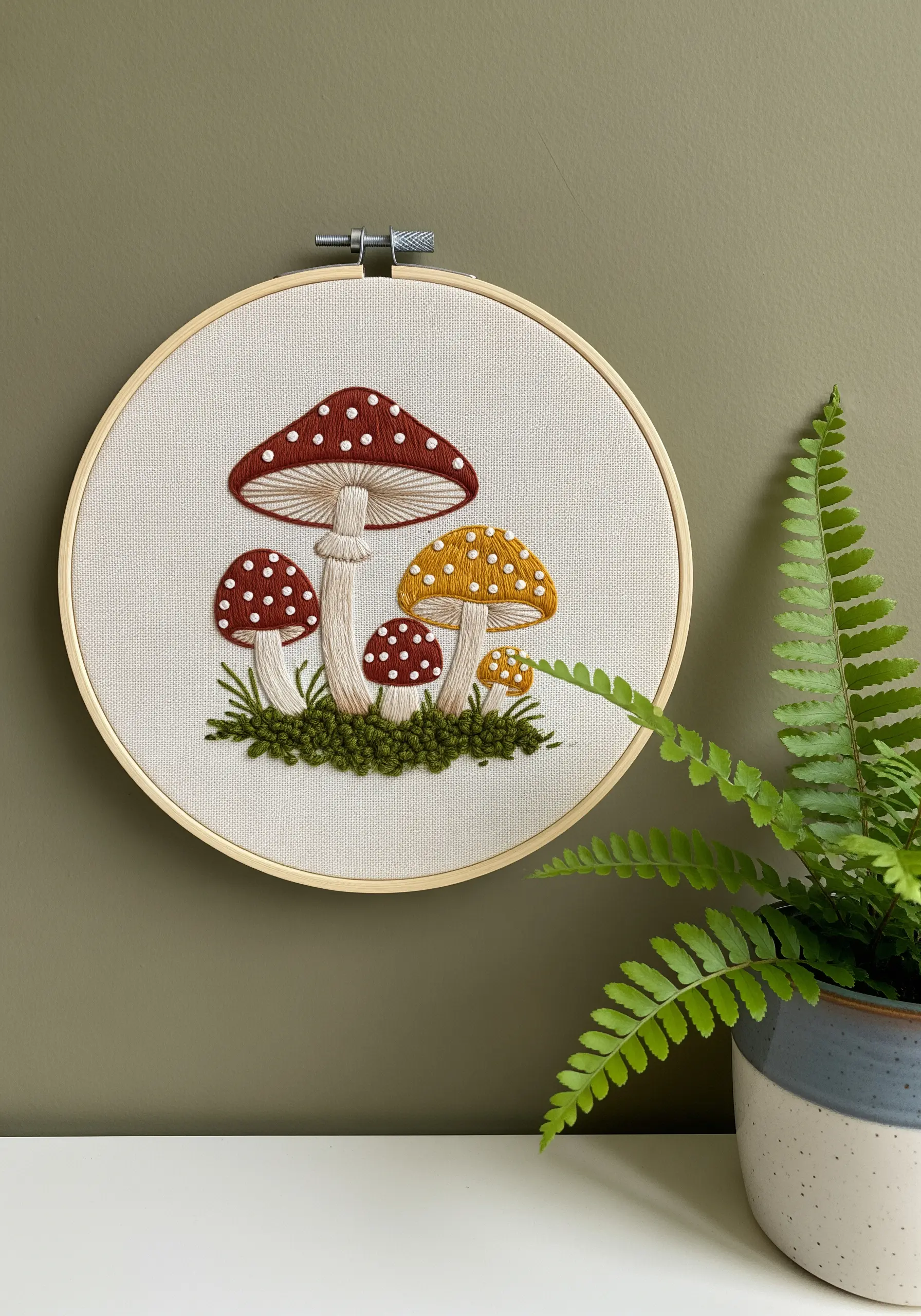 Embroidered red and yellow toadstools with white spots and textured green grass.
