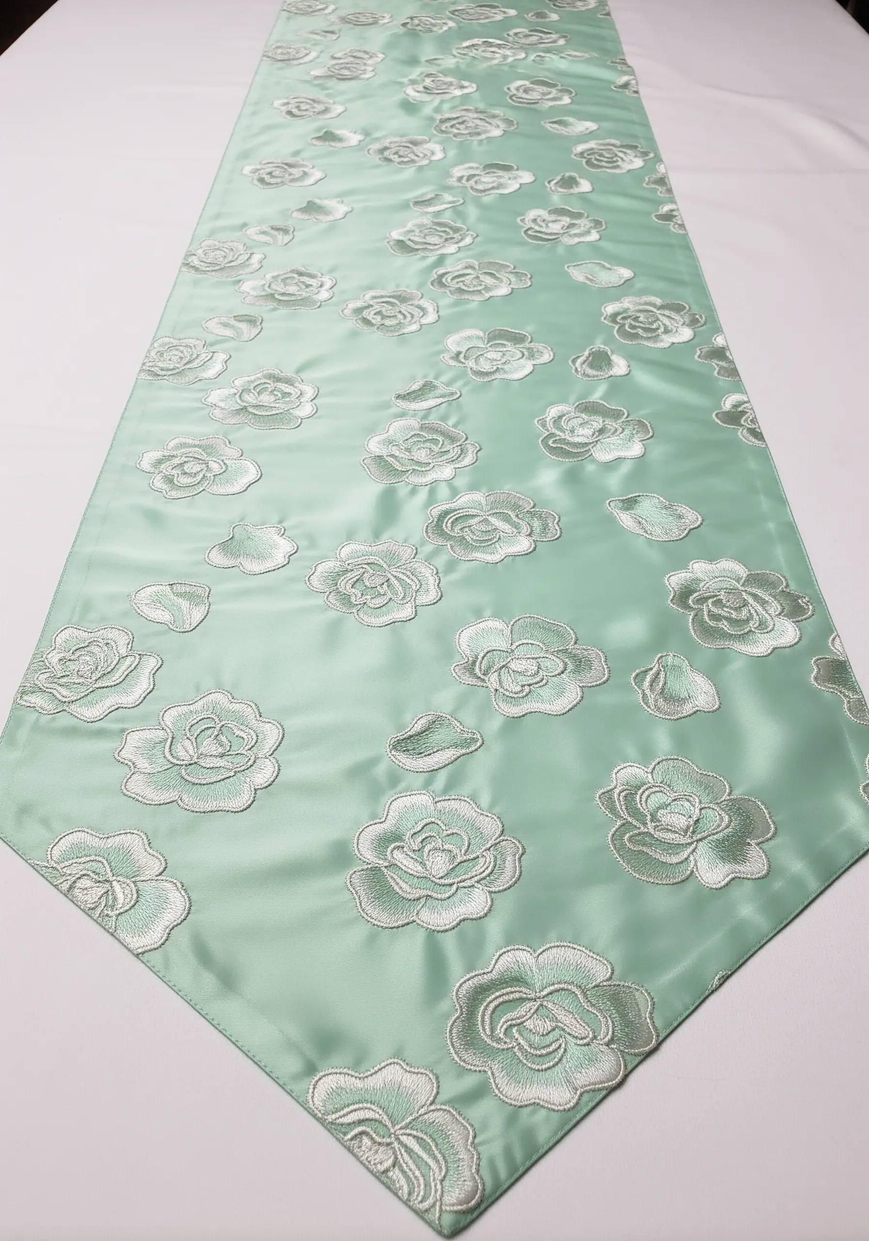 A mint green satin table runner with scattered roses embroidered in a slightly lighter green thread.