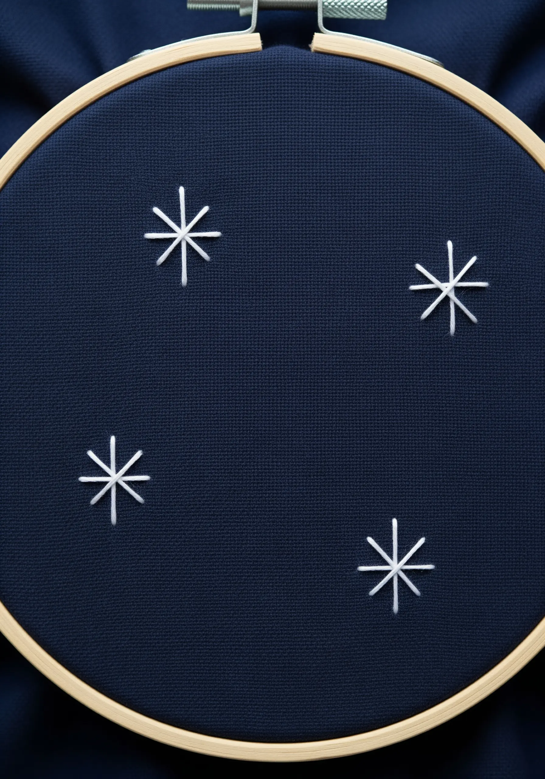Four minimalist star stitches in white thread on navy blue fabric.
