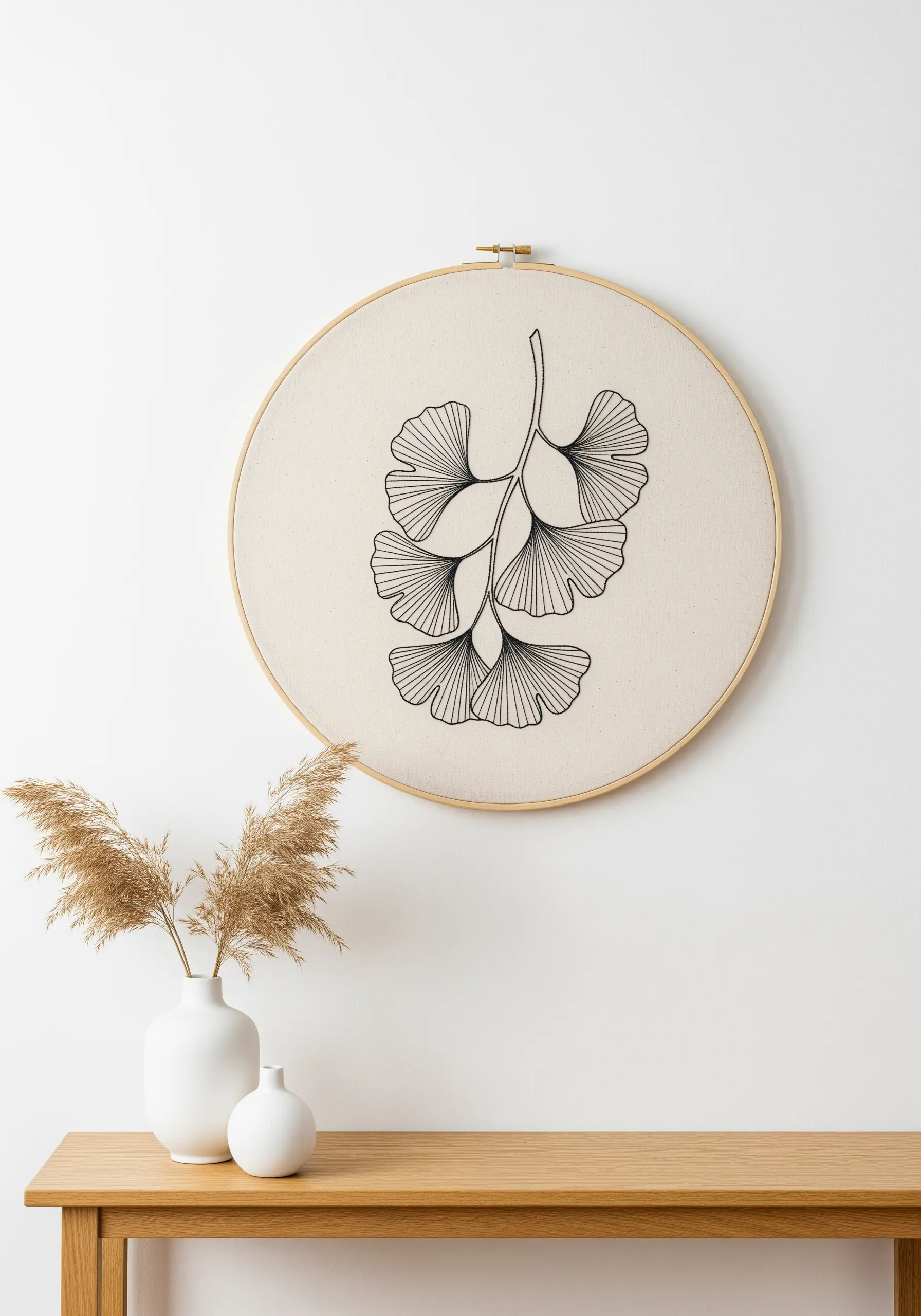 Minimalist black line embroidery of a ginkgo leaf branch in a wooden hoop.