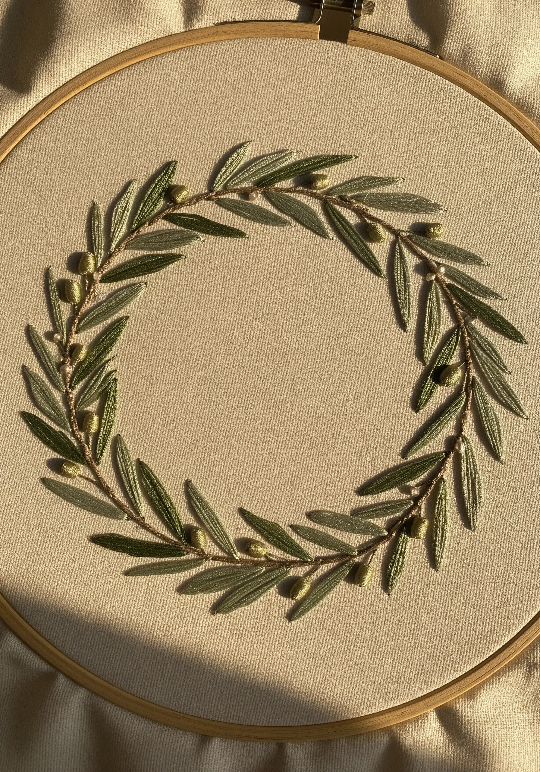 A delicate olive branch wreath embroidered in a hoop with green leaves and small knots for olives.