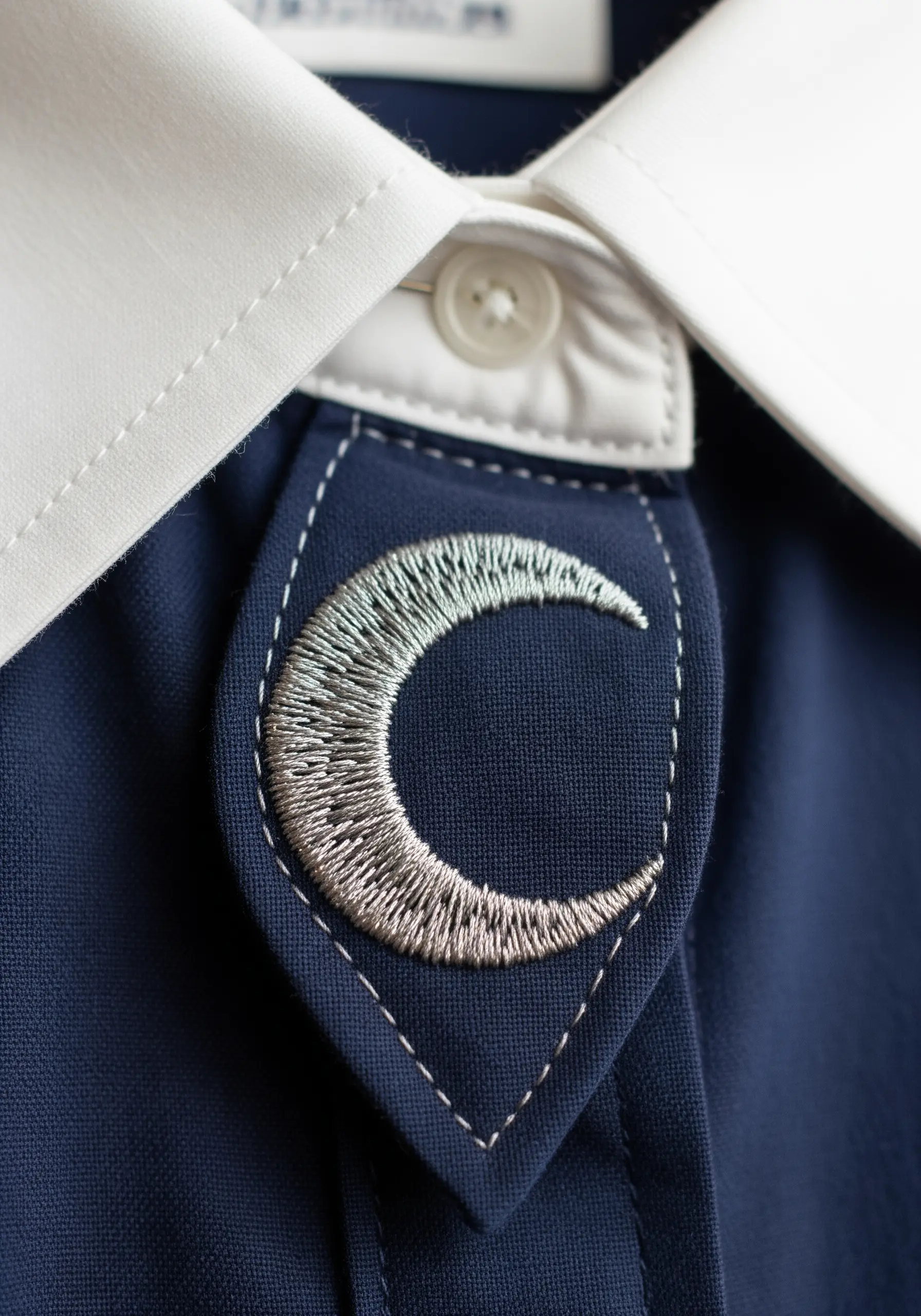 A crescent moon patch with a silver-to-gold metallic thread gradient on a shirt collar.