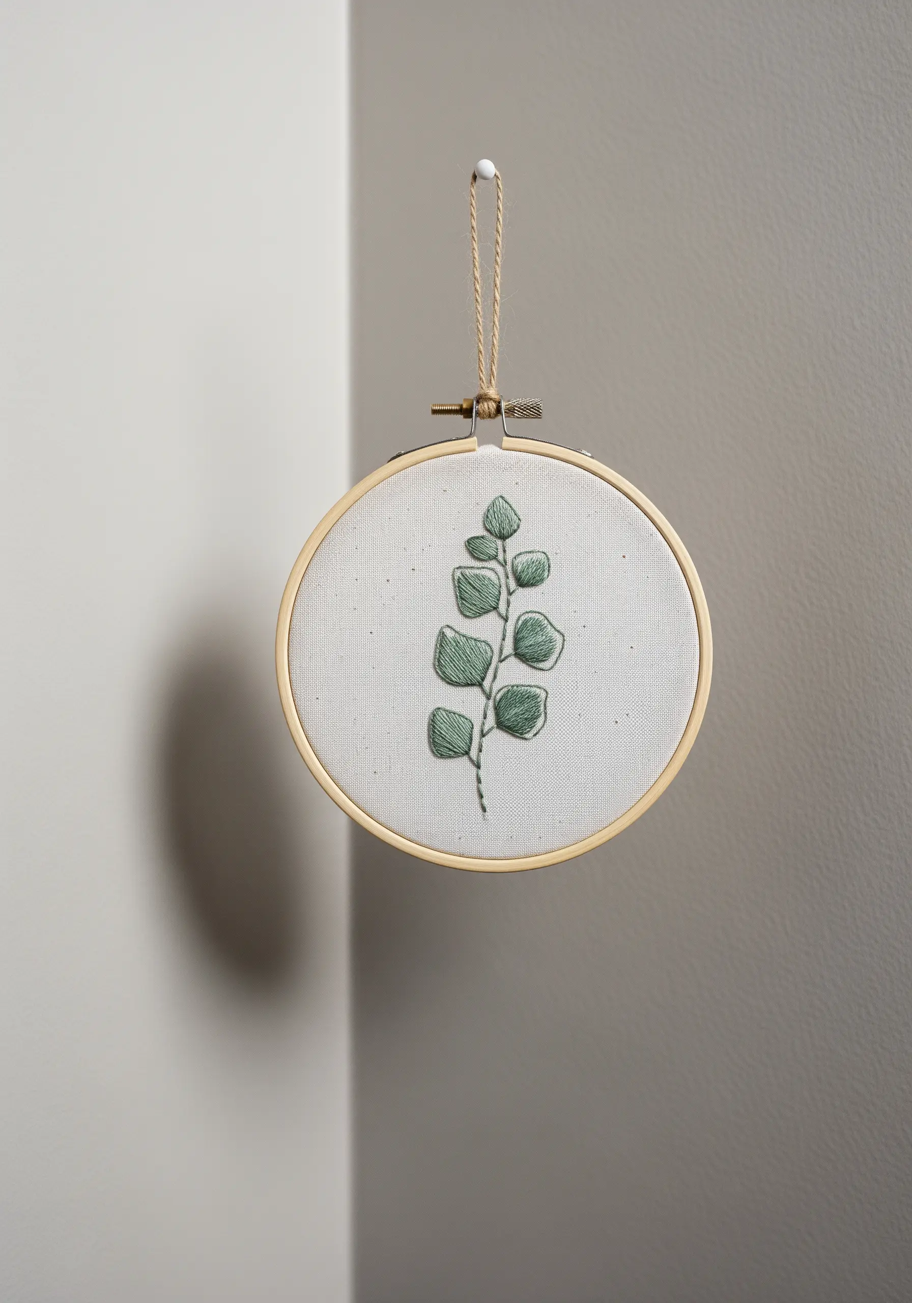 Eucalyptus branch with padded satin stitch leaves and outlined stem in an embroidery hoop.