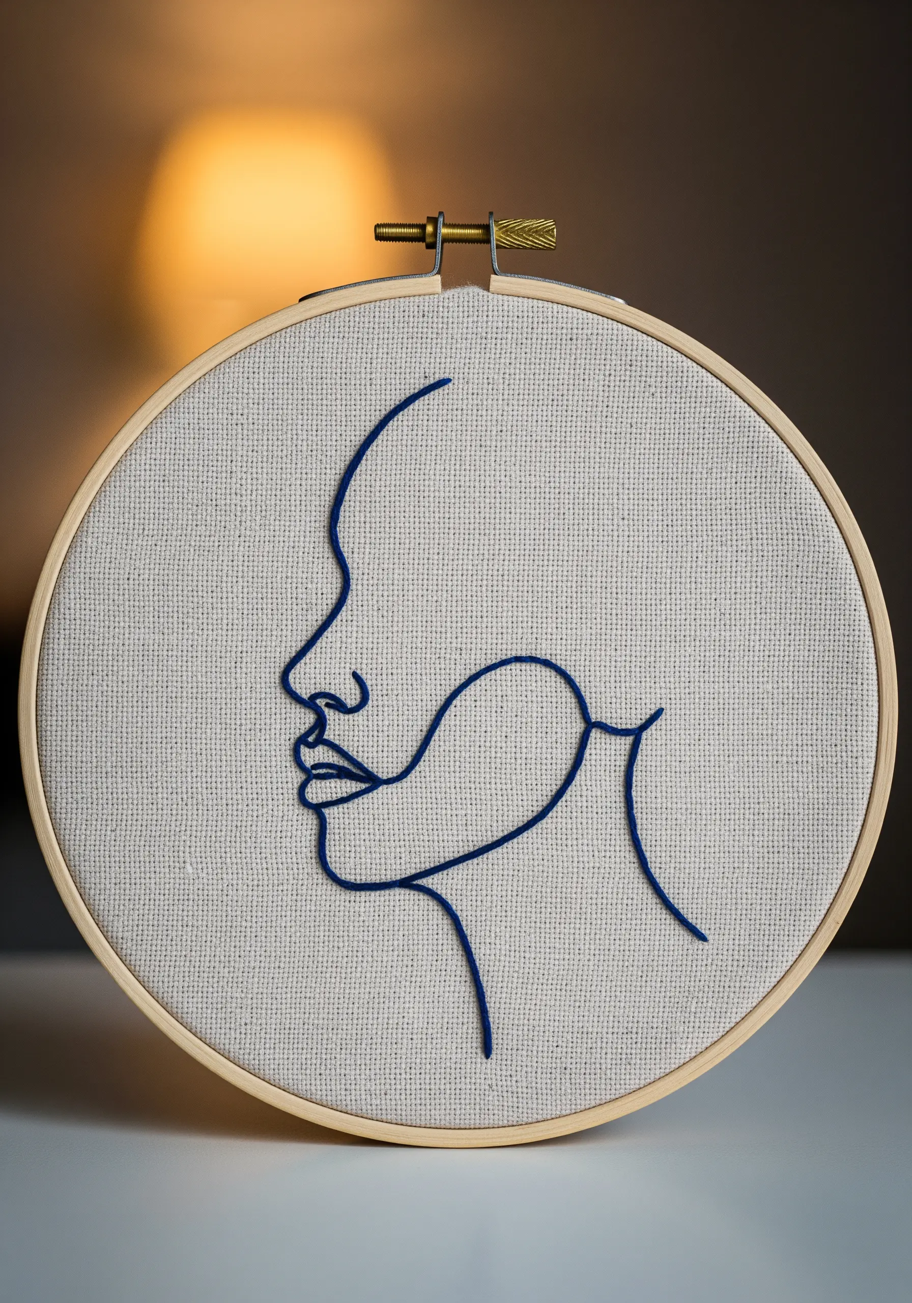 A minimalist one-line portrait of a face, stitched in dark blue thread on light fabric.