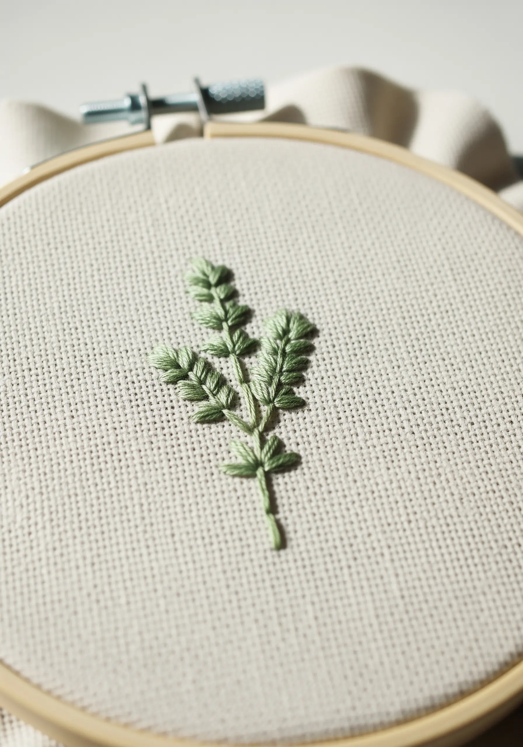 A small mint sprig embroidered in pale green, showcasing the texture of fishbone stitch leaves.