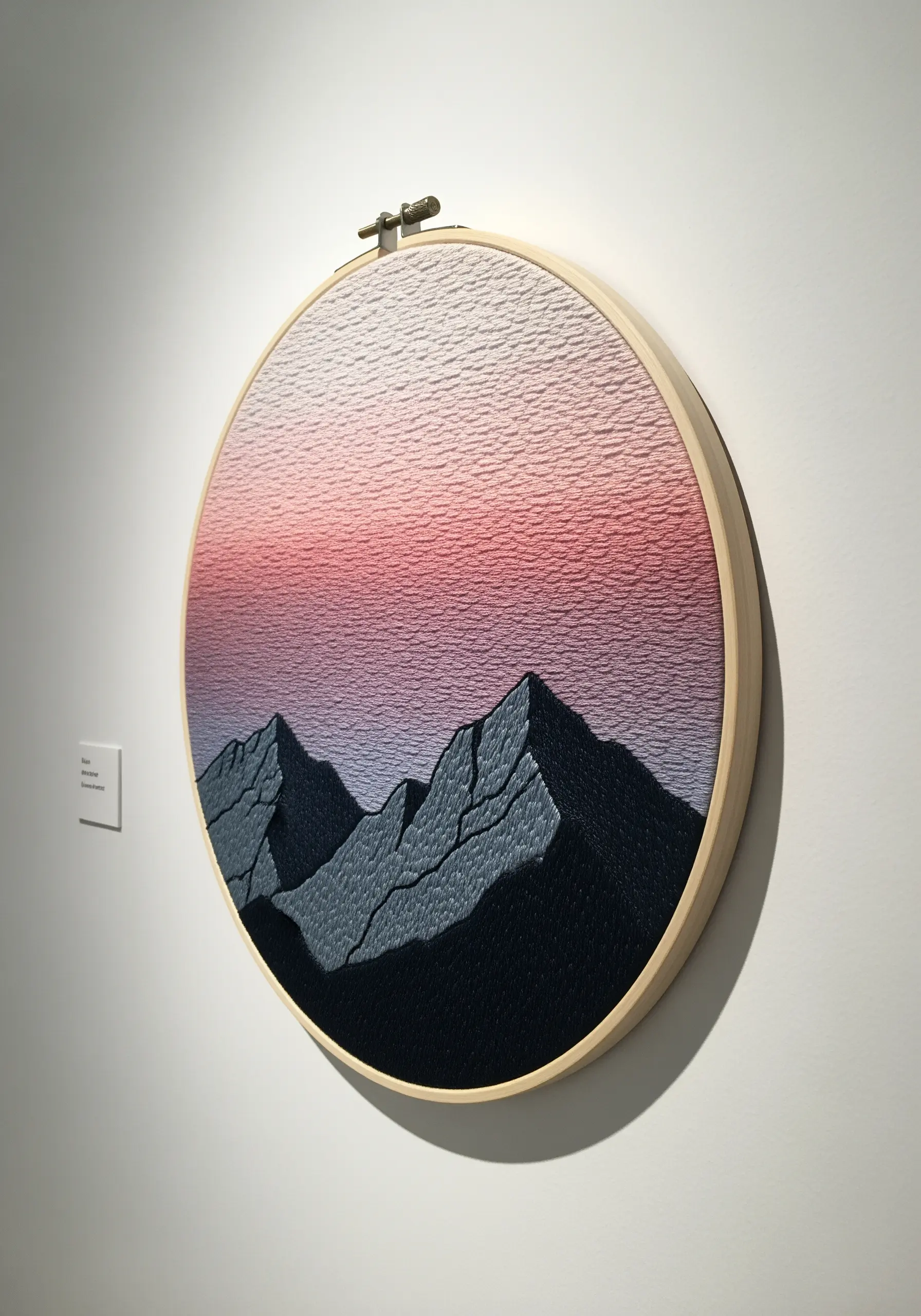 Embroidery hoop art of a mountain range with a pink and purple gradient sky created with thread painting.