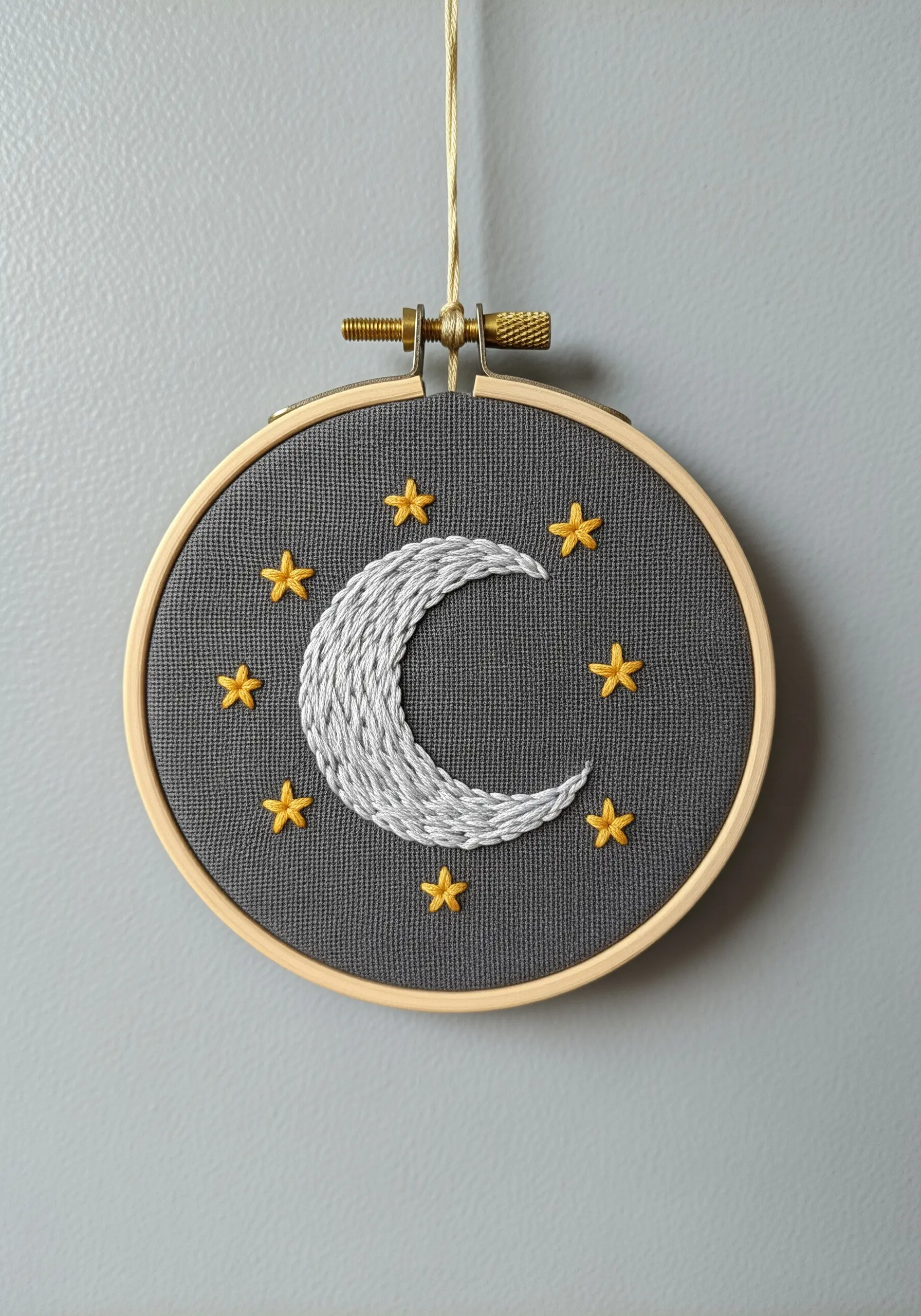 Embroidered crescent moon and yellow stars on a dark grey fabric in a hoop.