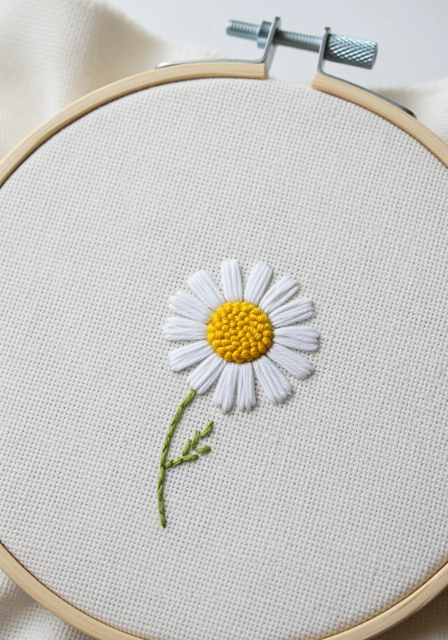 A single embroidered daisy with white satin stitch petals and a yellow French knot center.