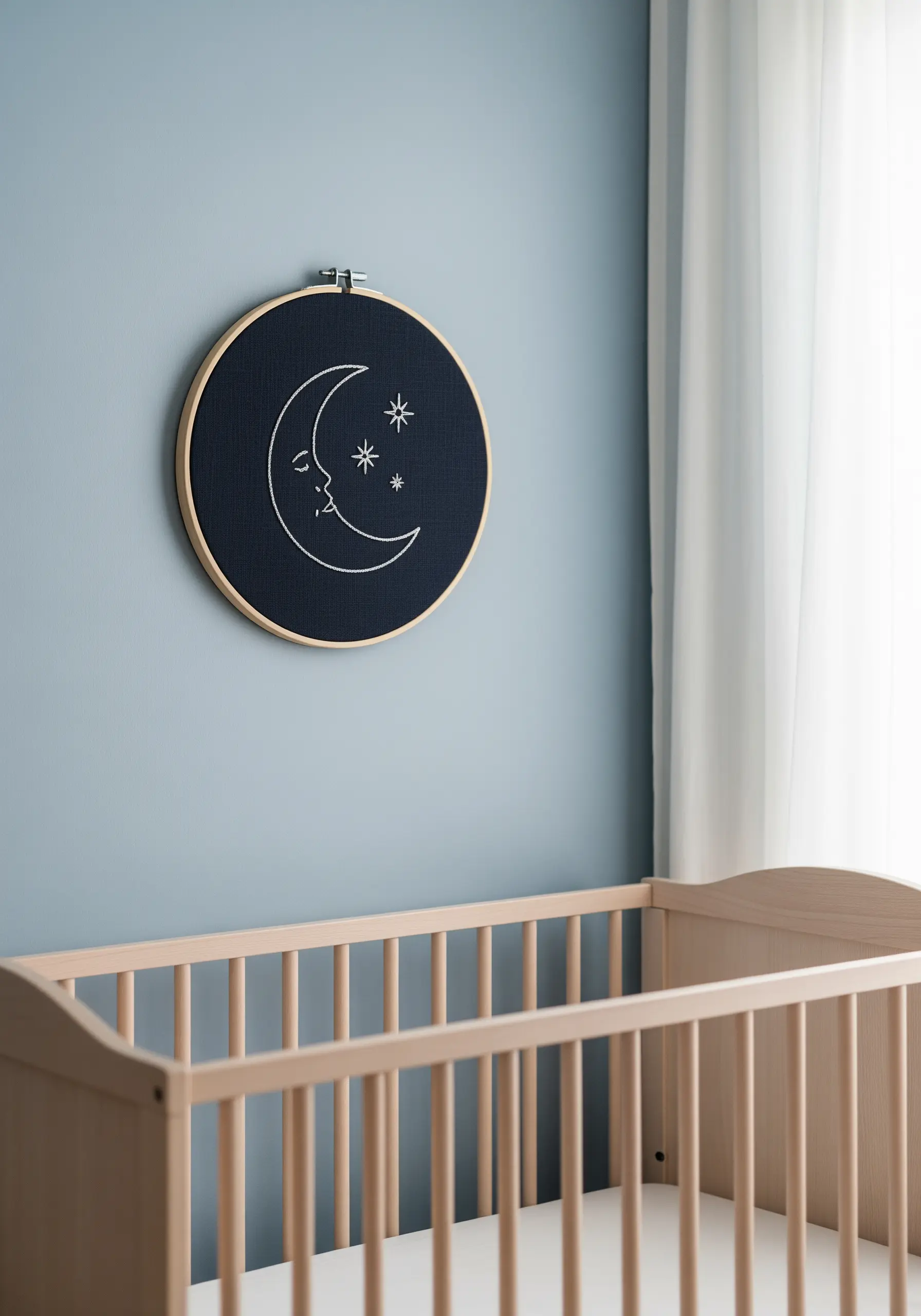 A crescent moon and stars embroidered in white thread on black fabric in a hoop.