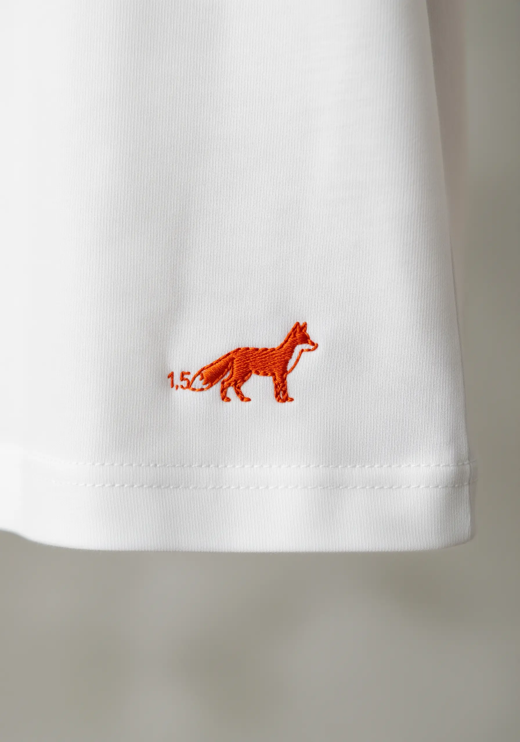 A tiny, detailed fox embroidered in orange on the sleeve hem of a t-shirt.