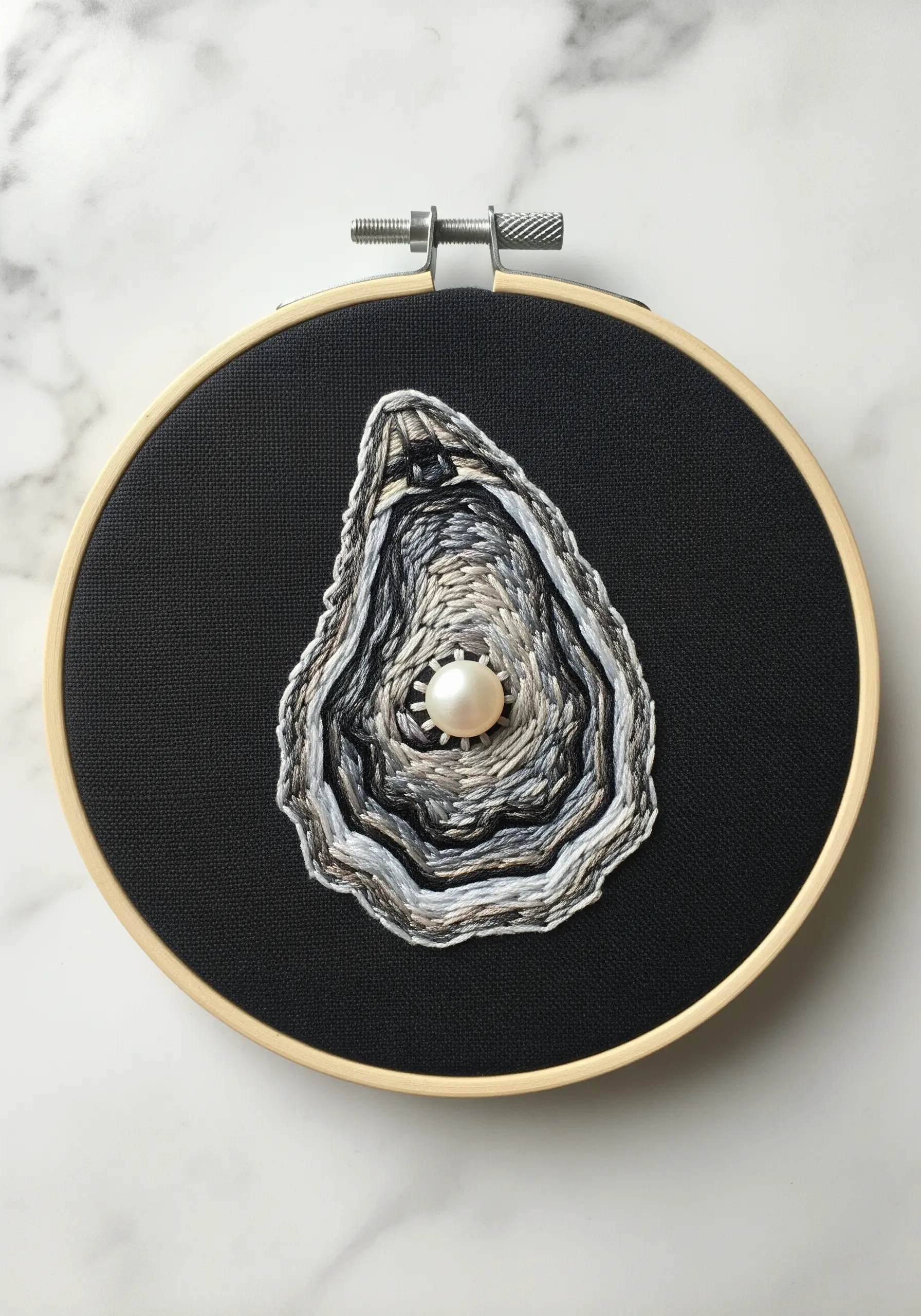 An oyster shell with a pearl, embroidered with detailed thread painting on black fabric.
