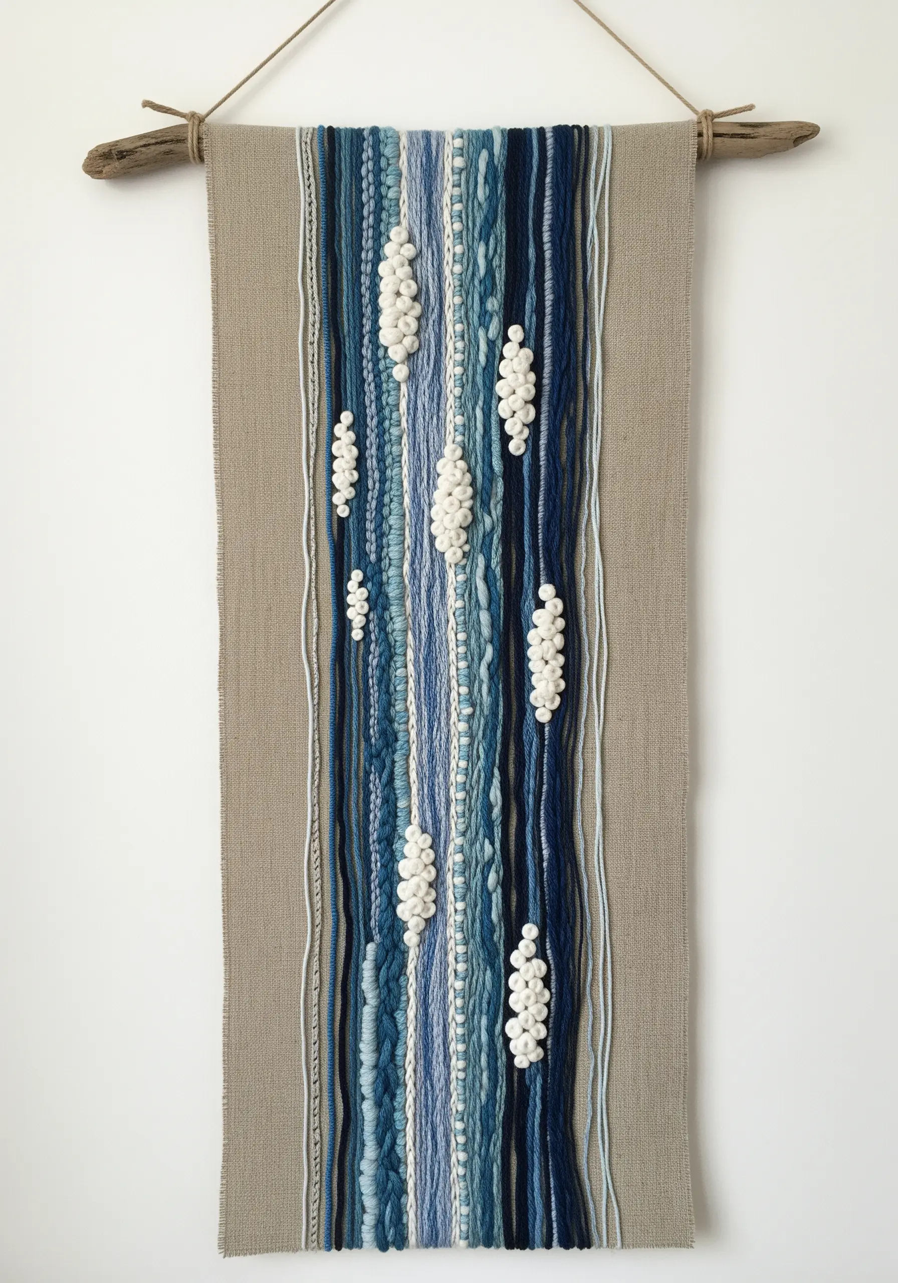 A woven-style wall hanging on linen, featuring blue yarns and textured white pom-pom clusters.