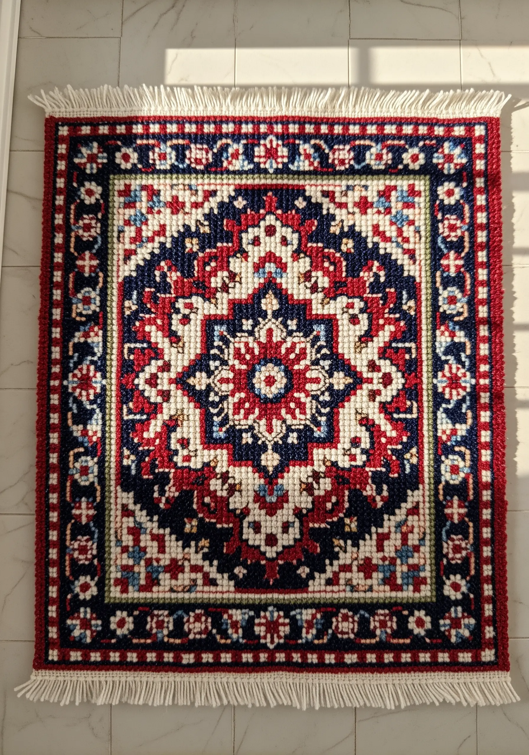 A small, intricately patterned rug made with red, white, and blue punch needle embroidery.
