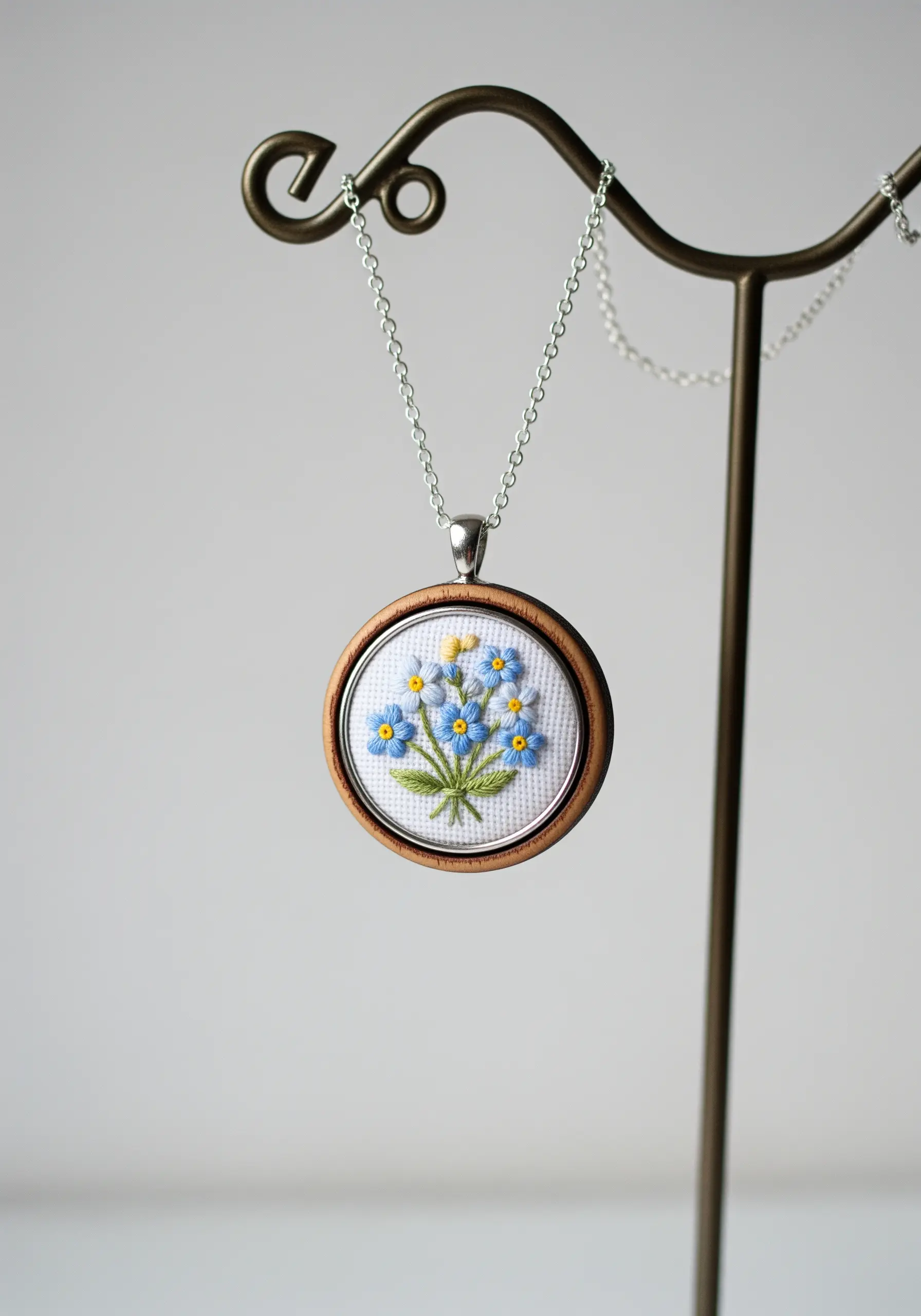 A tiny bouquet of embroidered forget-me-nots set inside a small wooden pendant necklace.