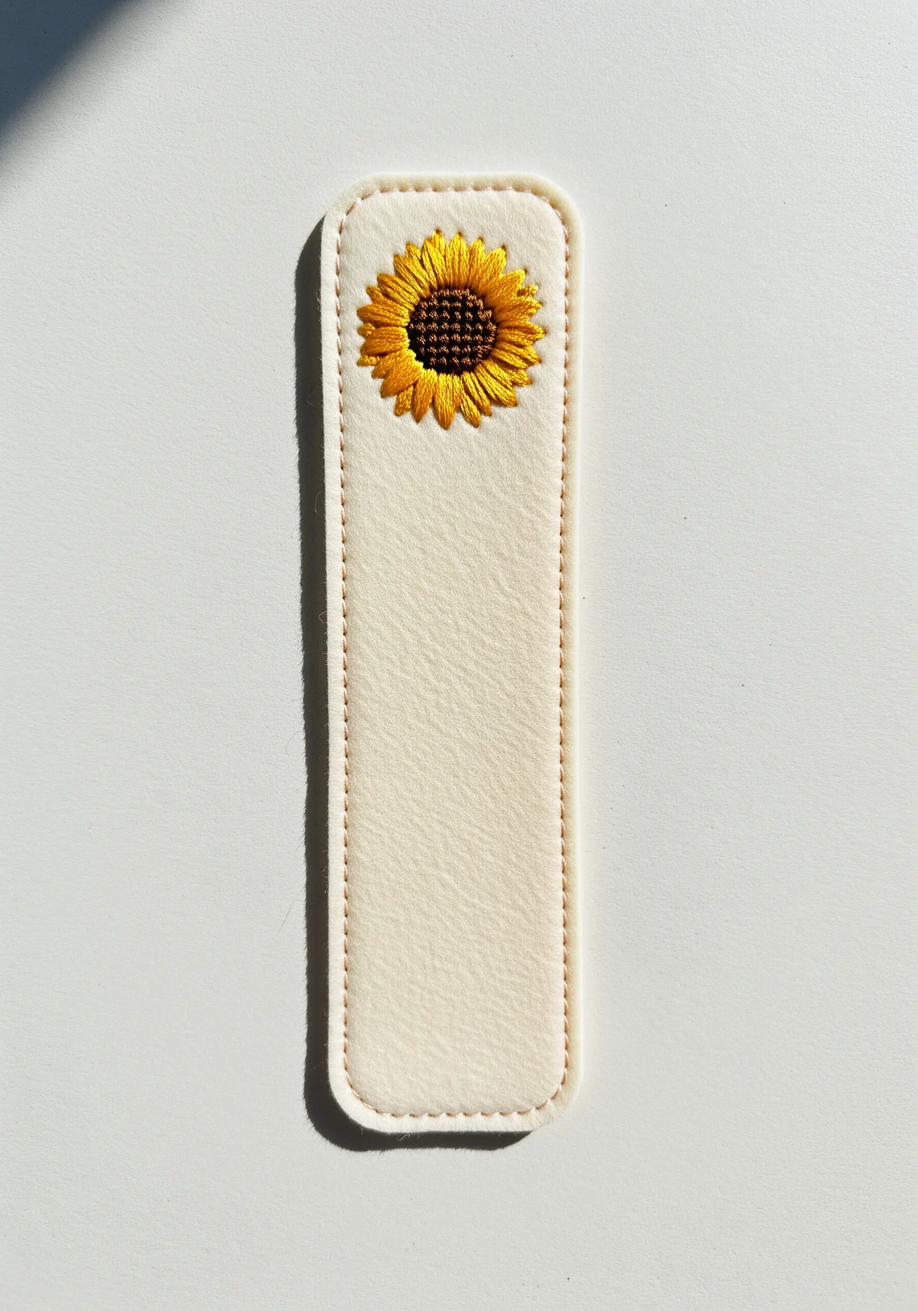 A small, realistic sunflower embroidered on a cream felt bookmark using thread painting.