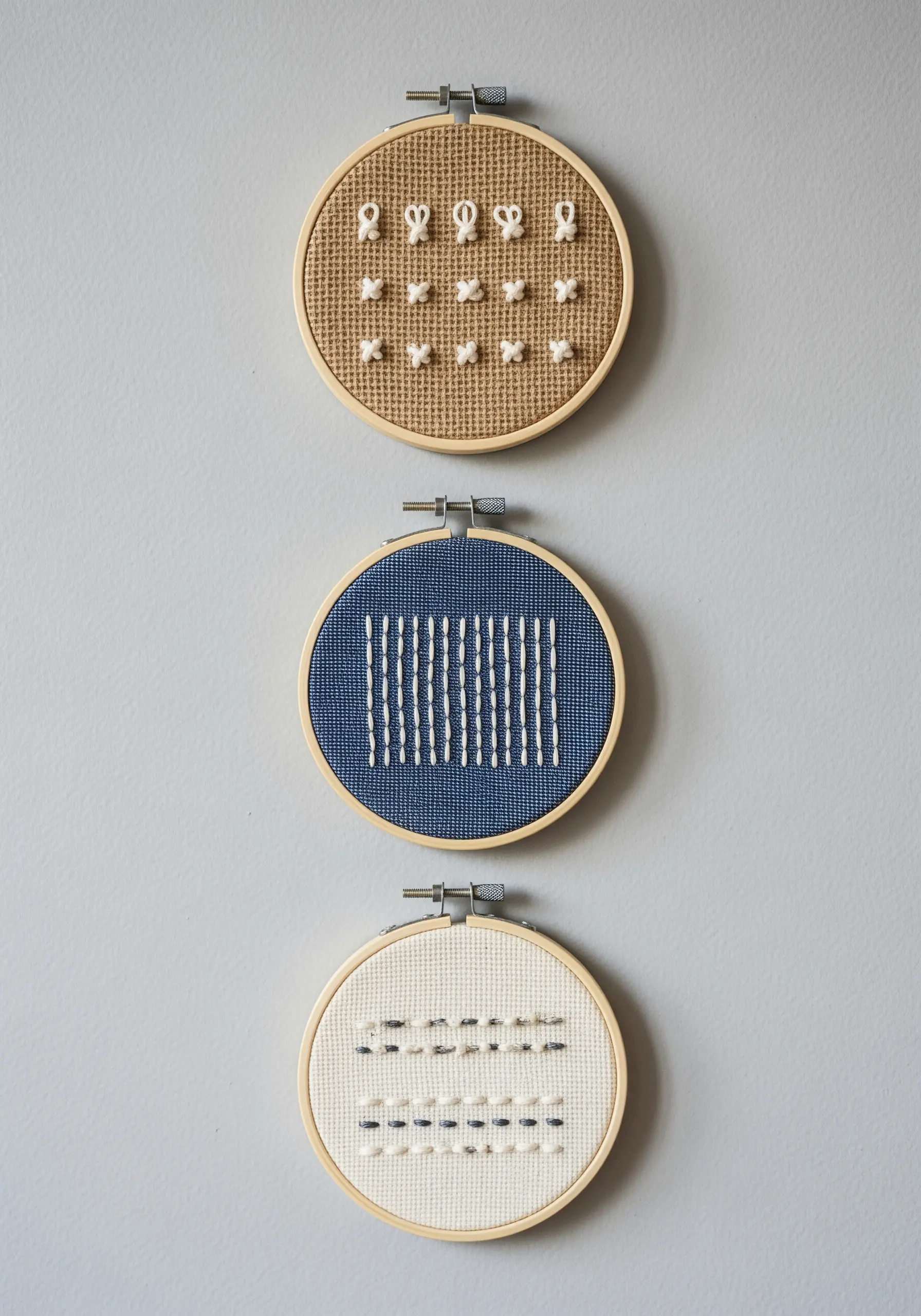 Three embroidery hoops showcasing simple, repeating stitches on different fabrics.