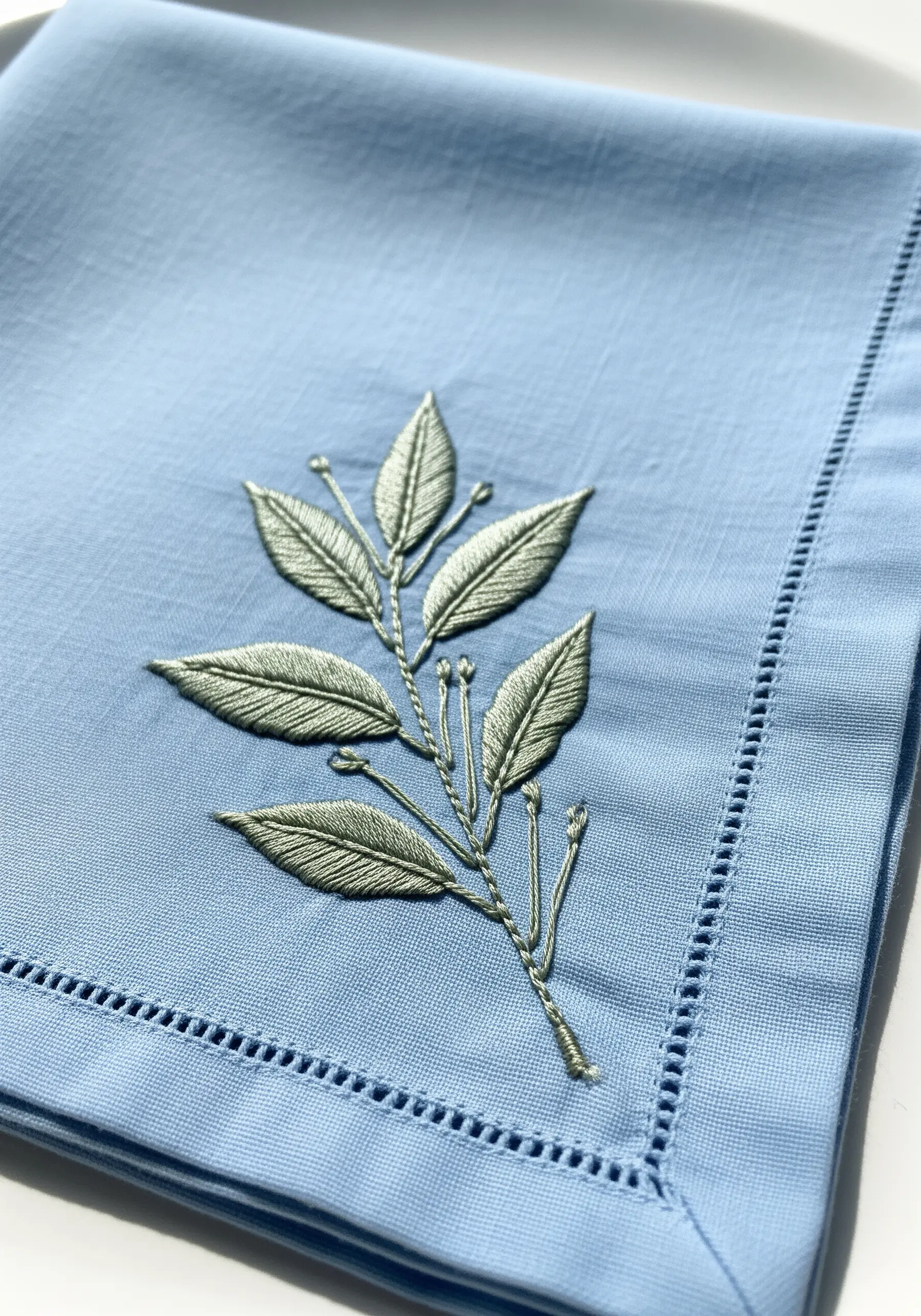 A single branch with leaves in silvery-green thread on a light blue napkin.