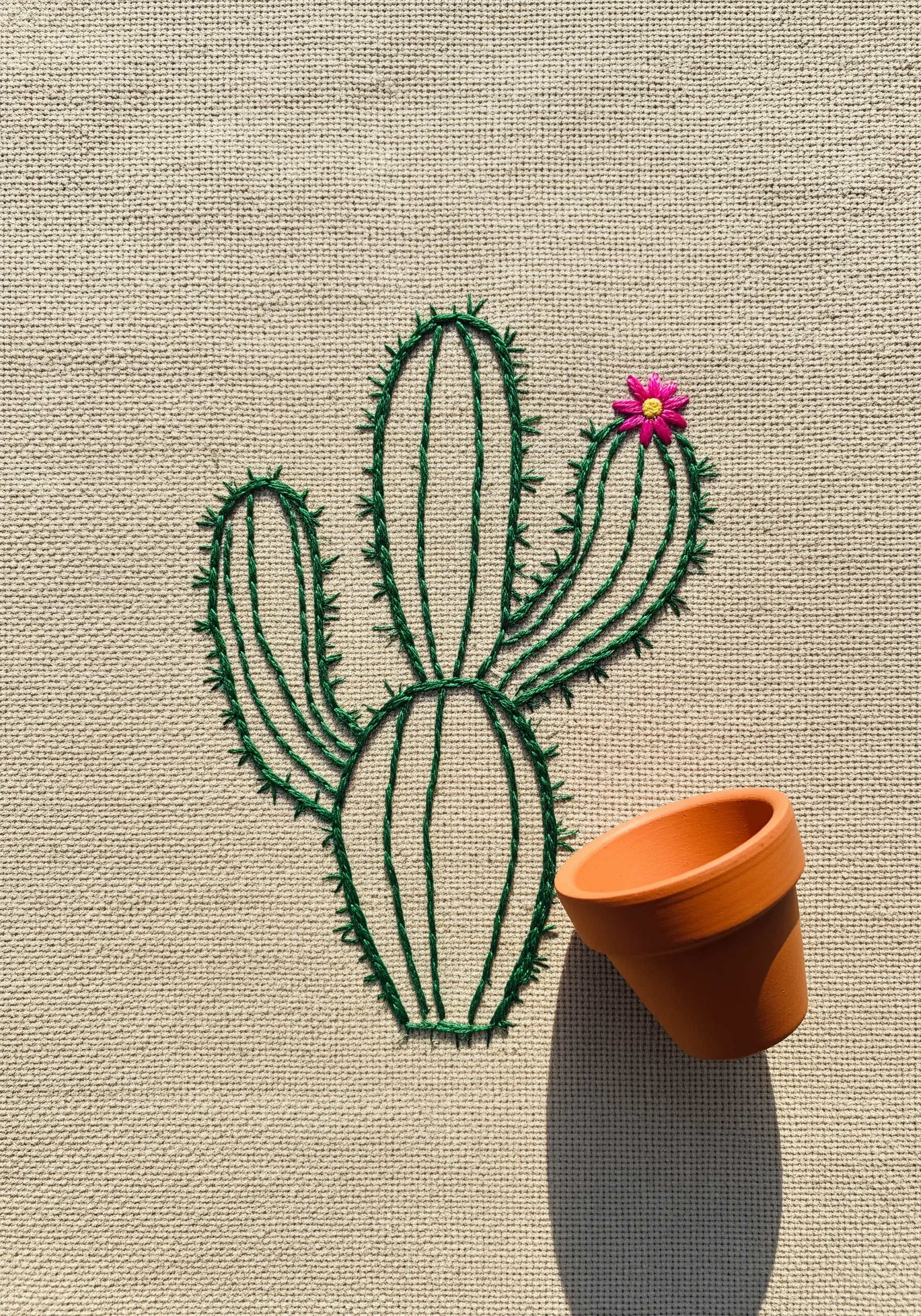 Green outline embroidery of a cactus with a real tiny clay pot