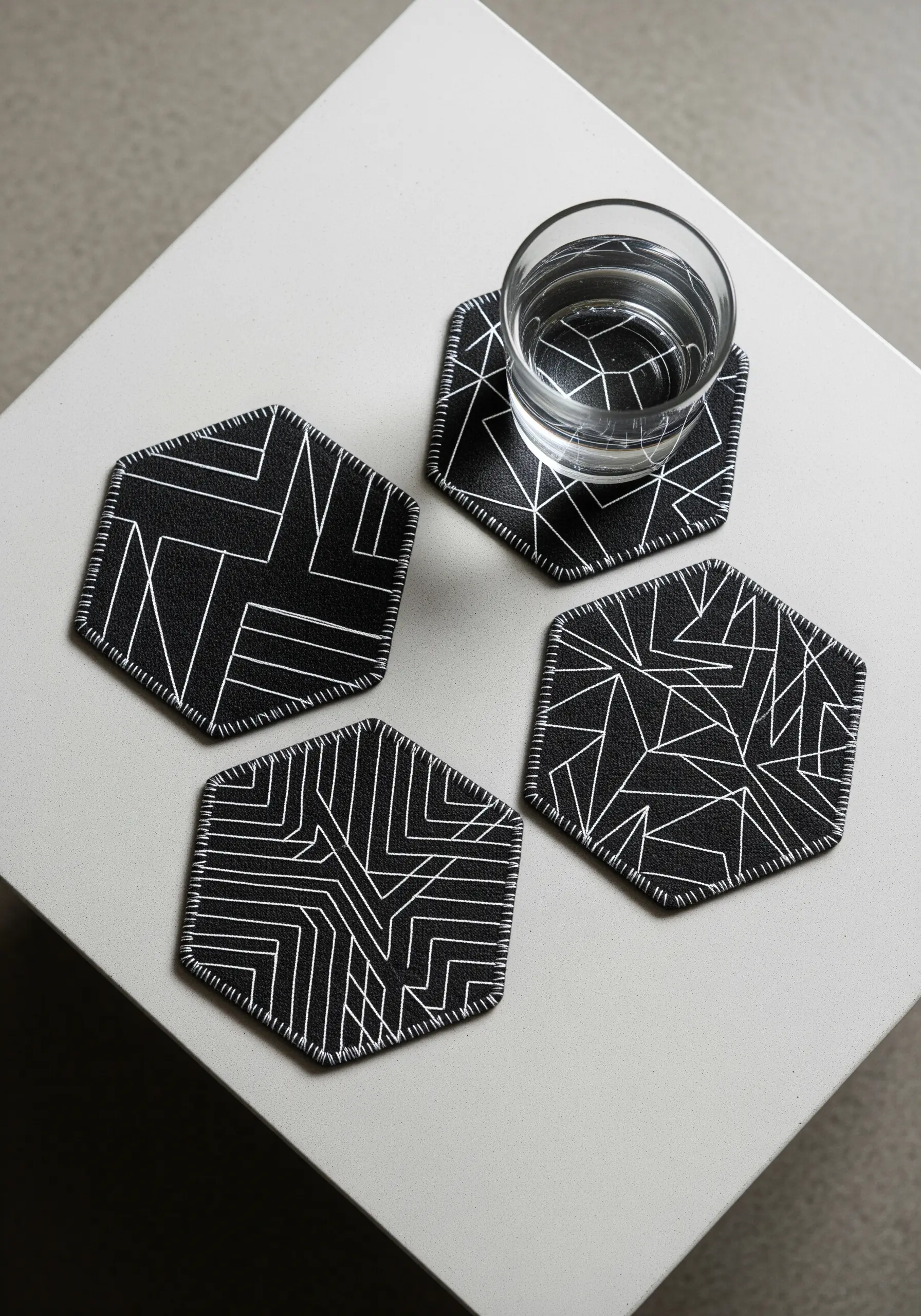 A set of four black hexagonal coasters with white geometric line embroidery.
