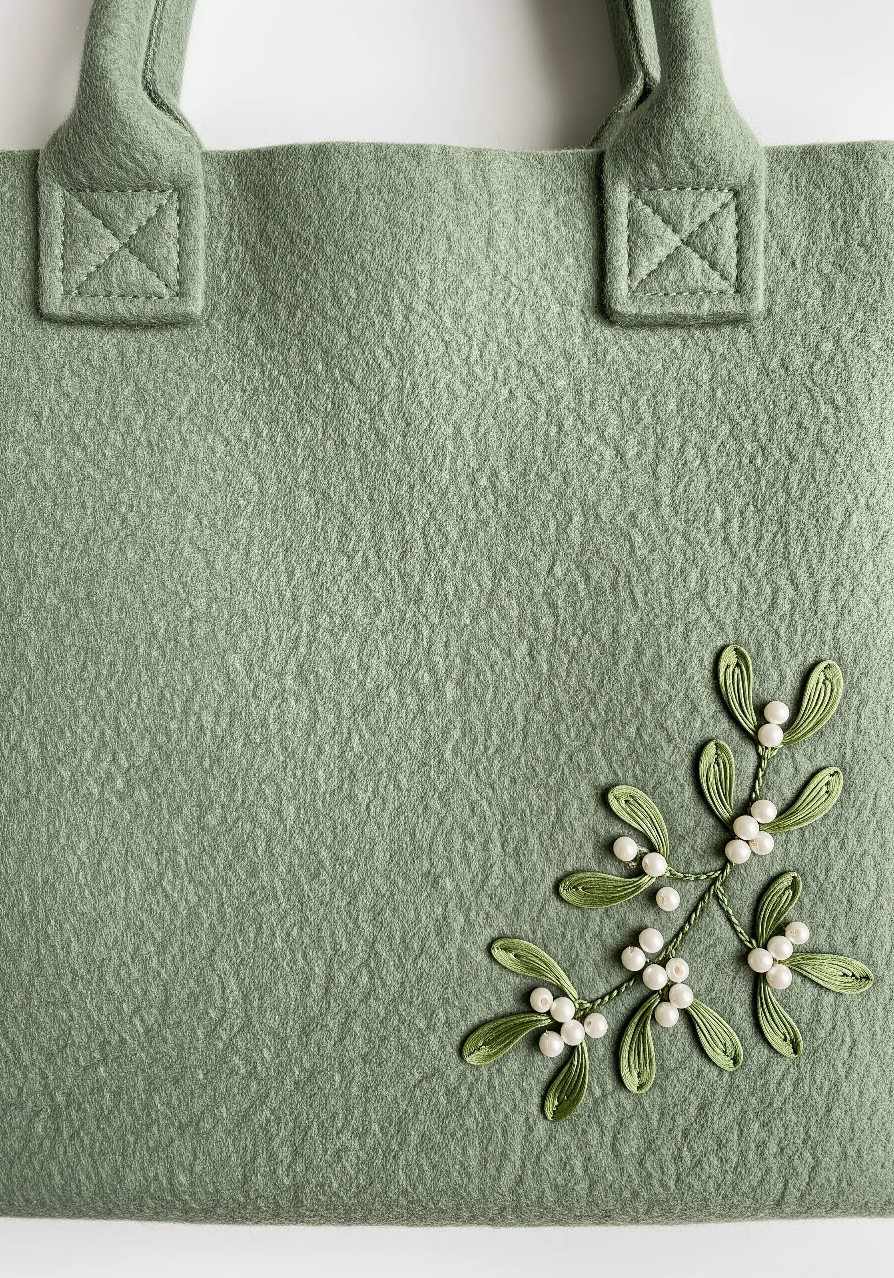 A delicate sprig of embroidered mistletoe with pearl beads for berries on a sage green felt tote.