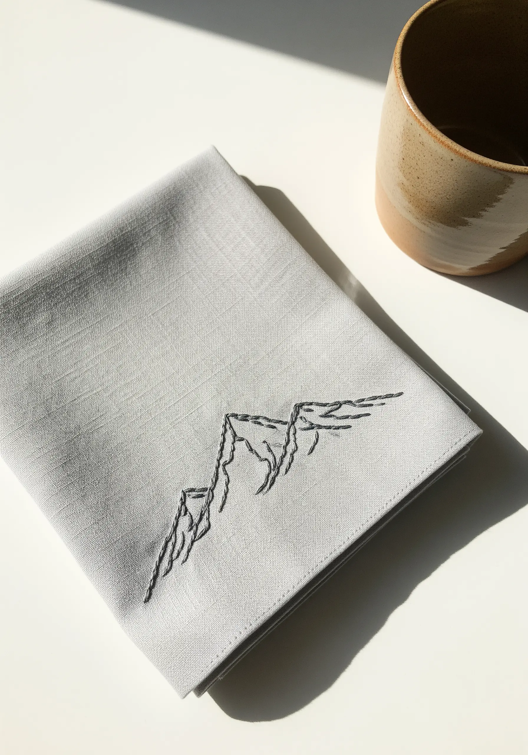 A minimalist line art mountain range embroidered in charcoal thread.