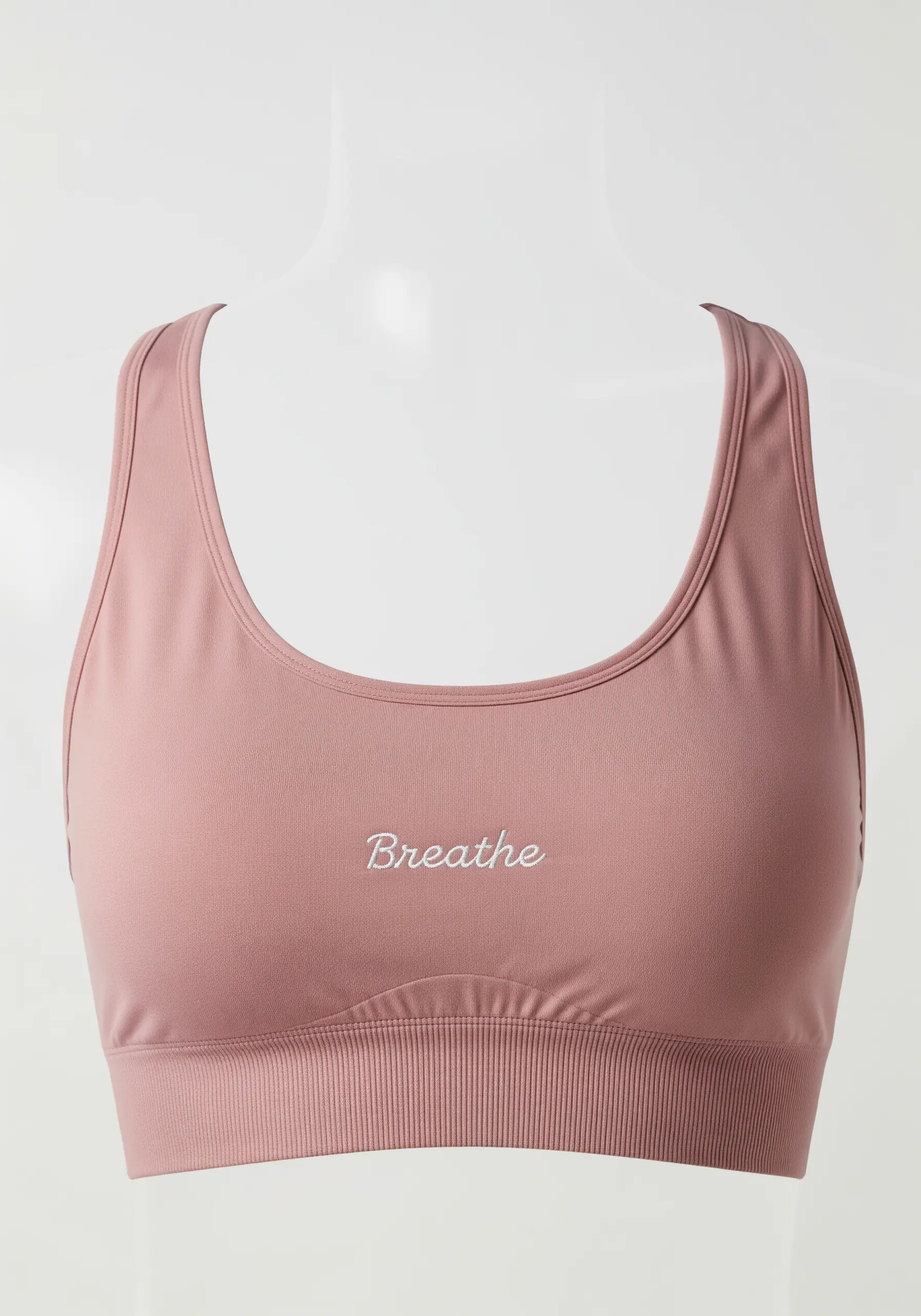 The word “Breathe” in fine white script on the chest of a dusty rose sports bra.