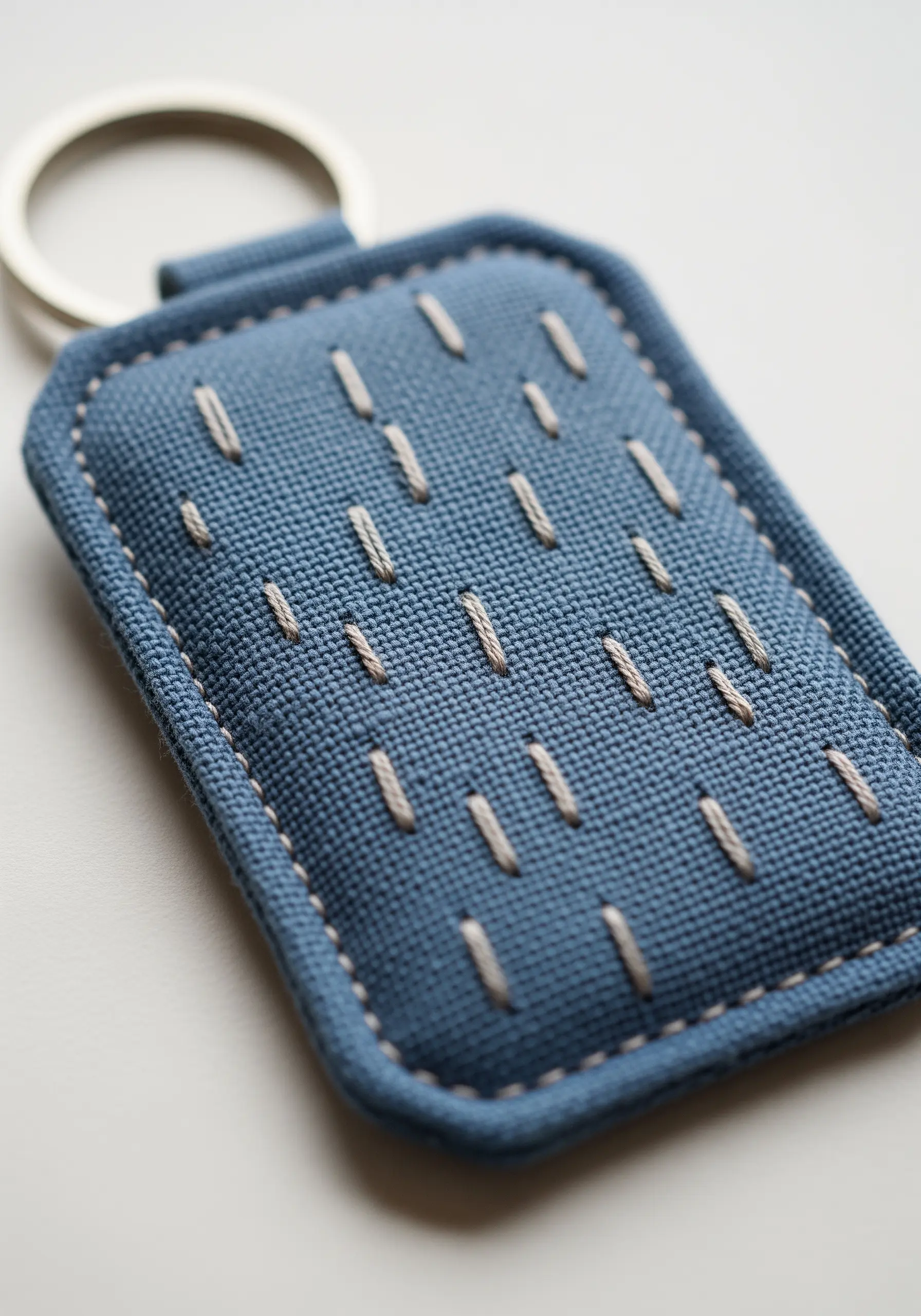 A blue fabric keychain decorated with a simple pattern of white seed stitches