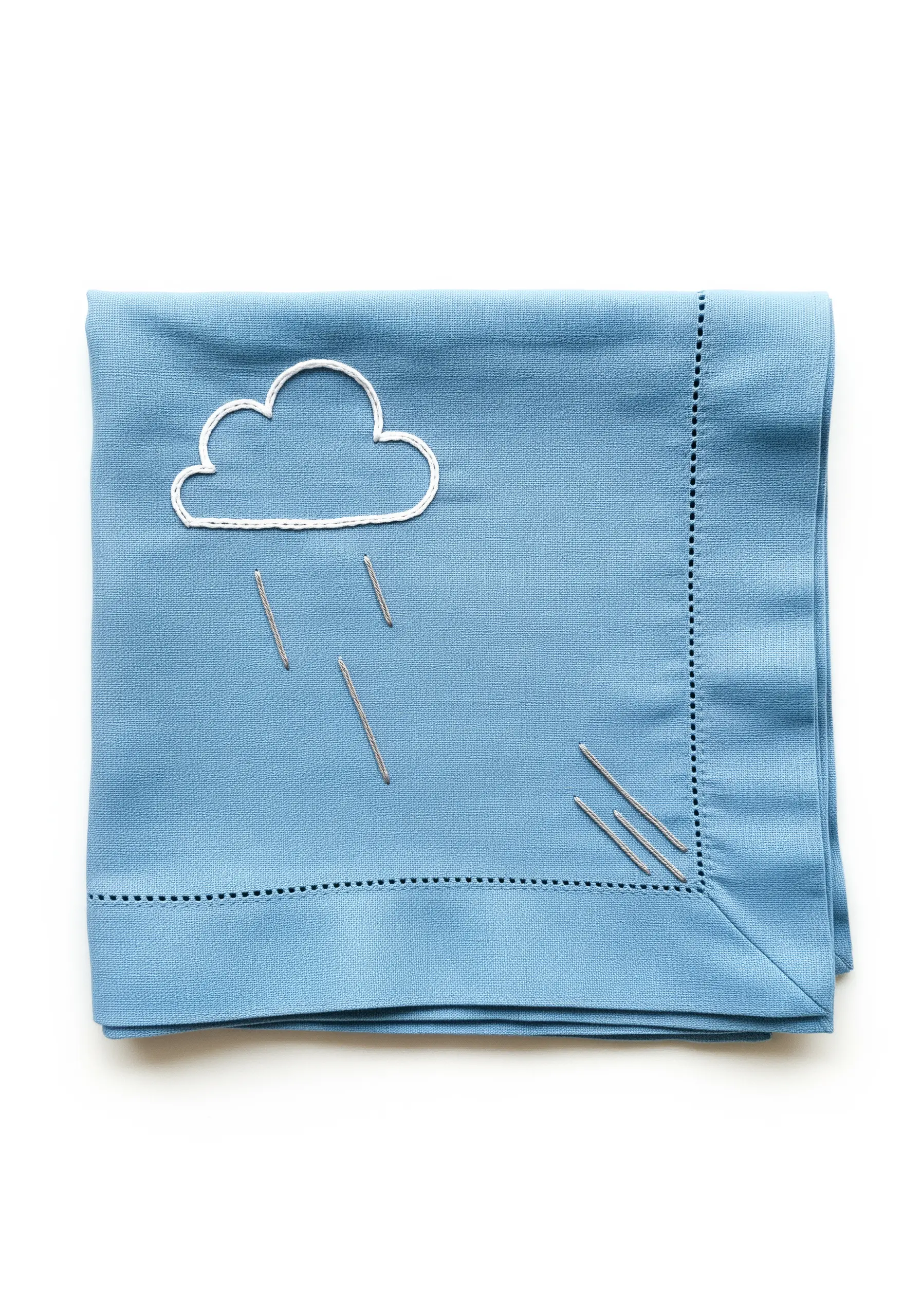 A simple embroidered cloud with straight-stitch raindrops on a light blue napkin.