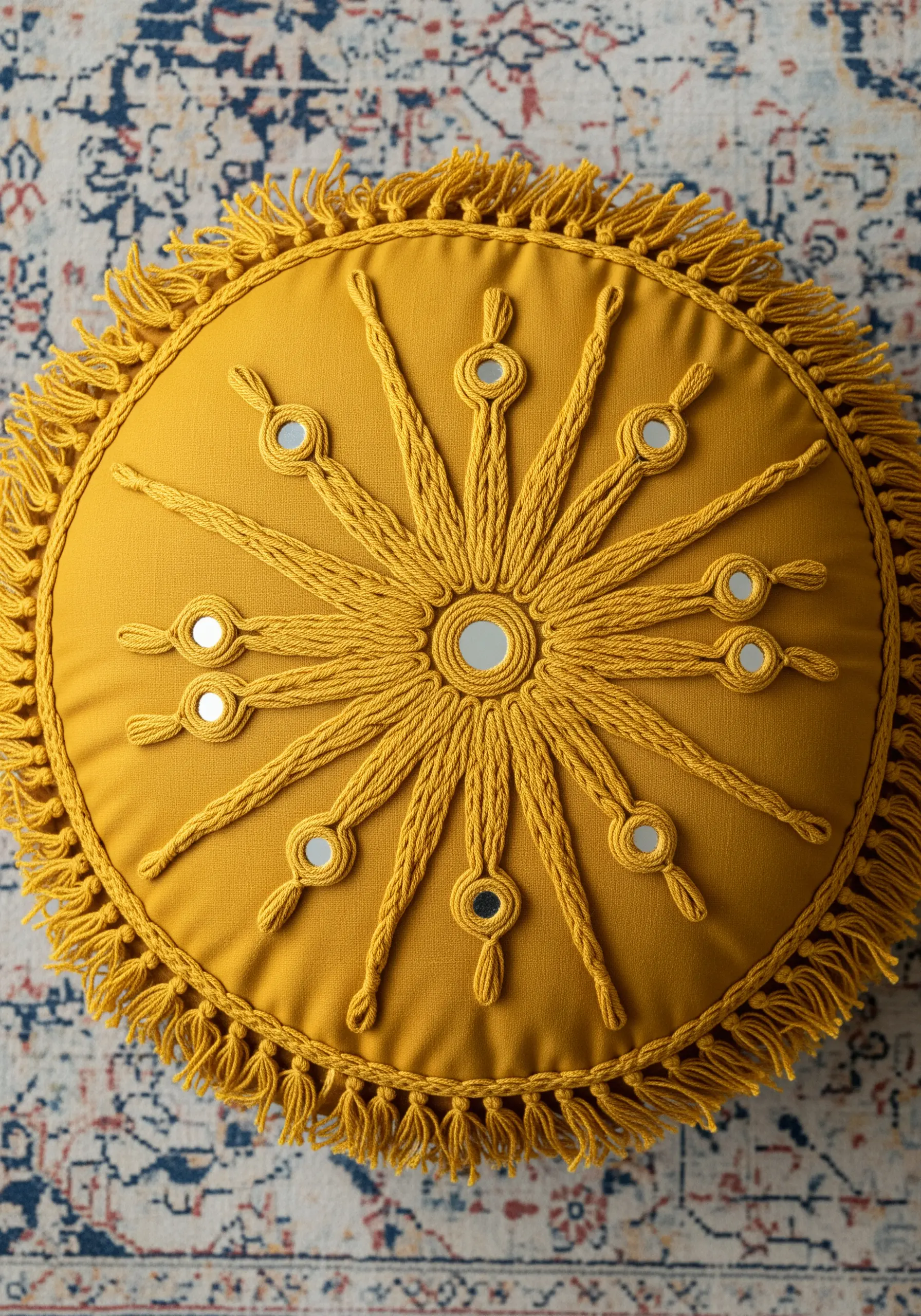Yellow round pillow with a couched yarn sunburst design and small mirrors.
