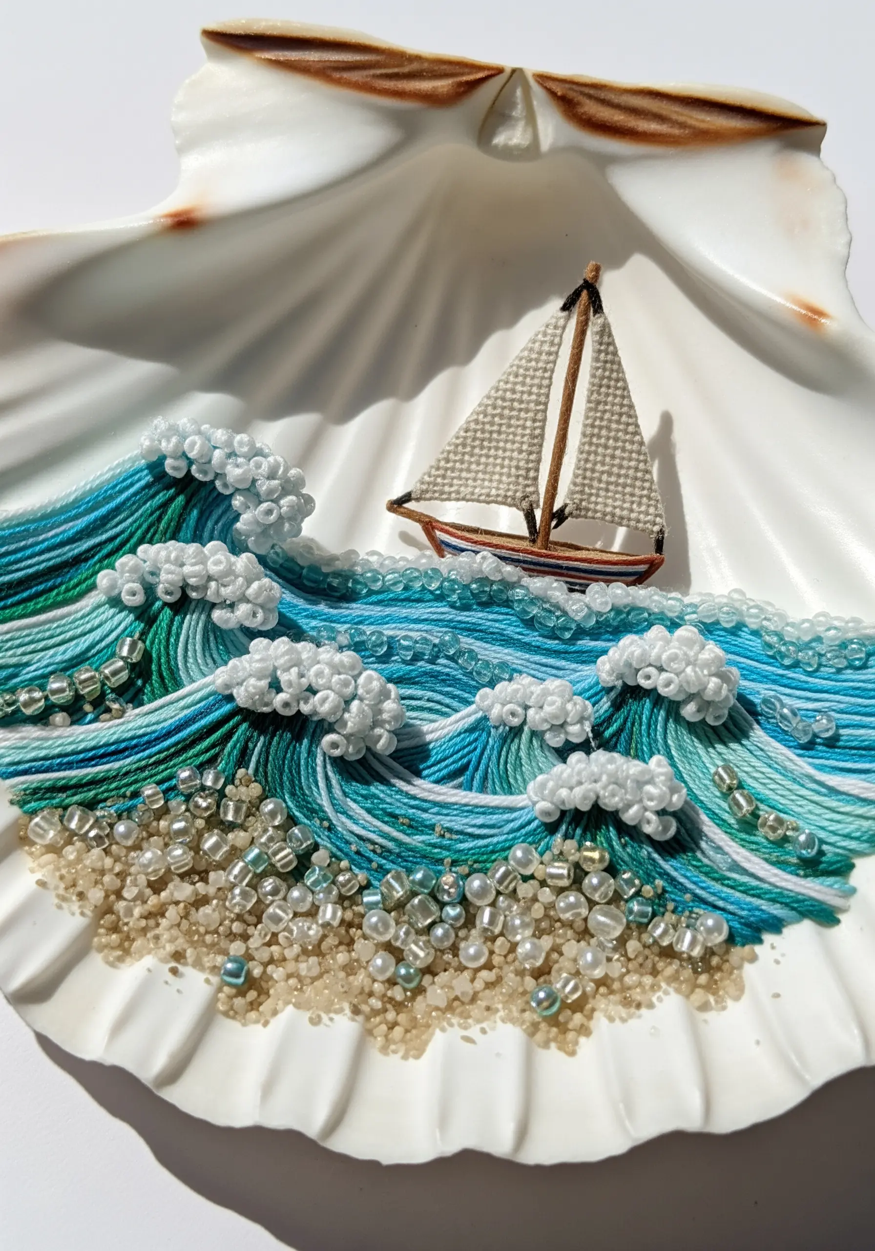 An embroidered ocean scene with thread waves and beaded sea foam inside a large seashell.